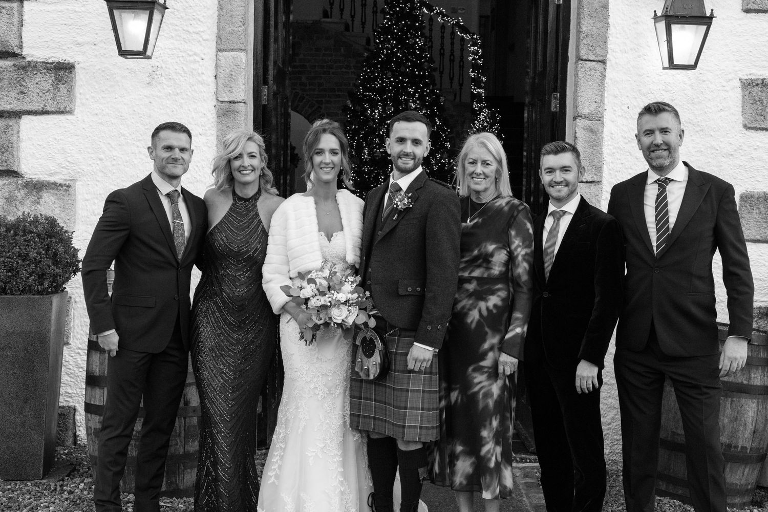 Wedding party poses for formal photos outside a traditional stone building with lanterns.