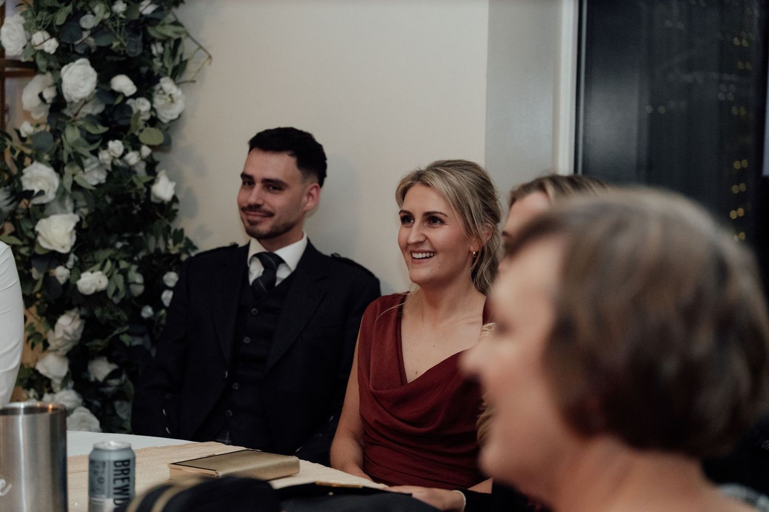 Wedding guests seated at tables during an elegant indoor reception with floral decorations.