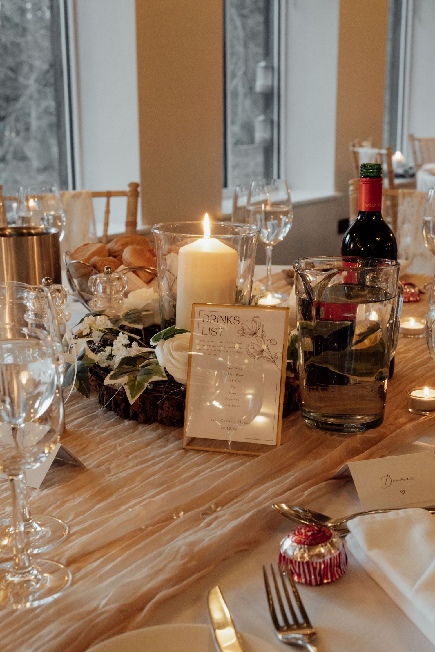 Wedding reception table setting with candles, wine glasses and rustic wooden details.