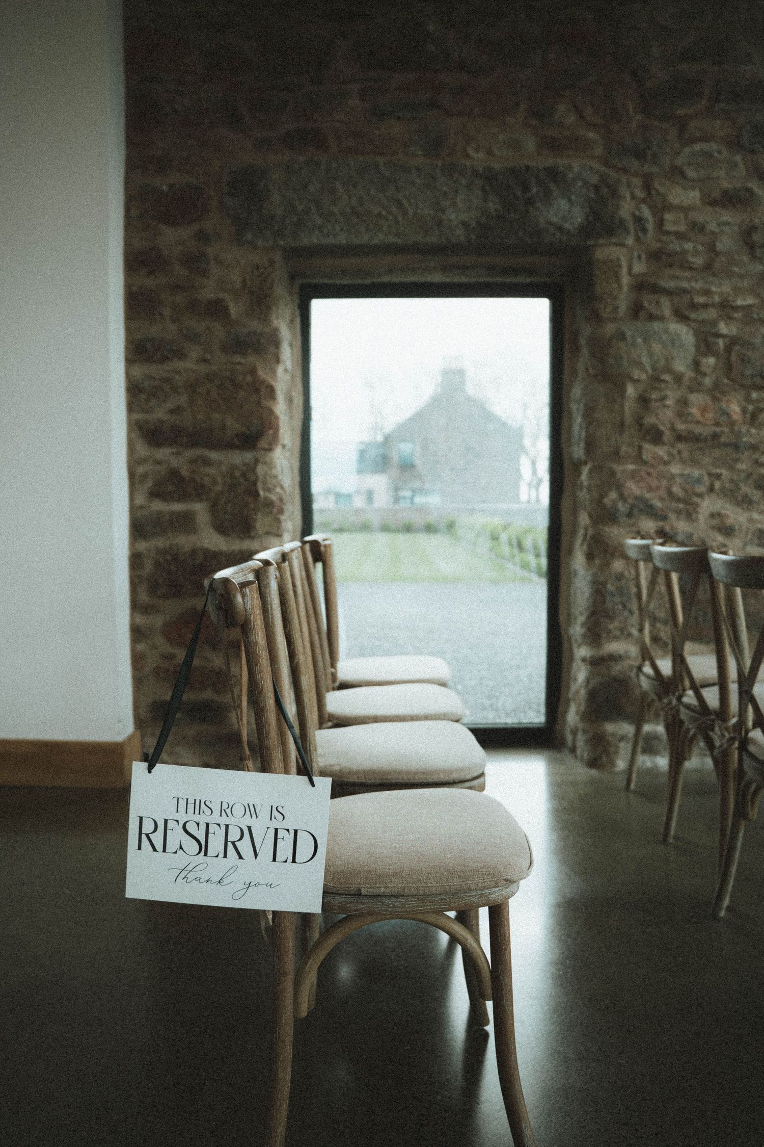 Reserved row sign on rustic wooden chairs in a stone-walled wedding venue ceremony space.