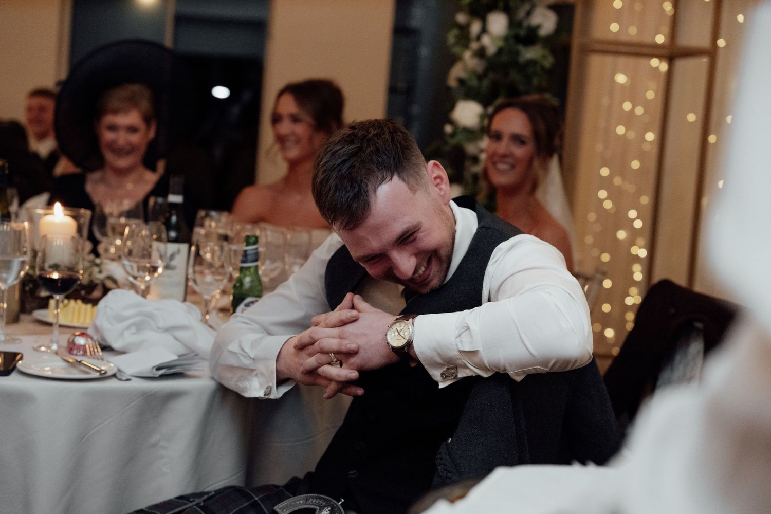 Reception guests enjoy candlelit dinner under twinkling lights and floral decorations.