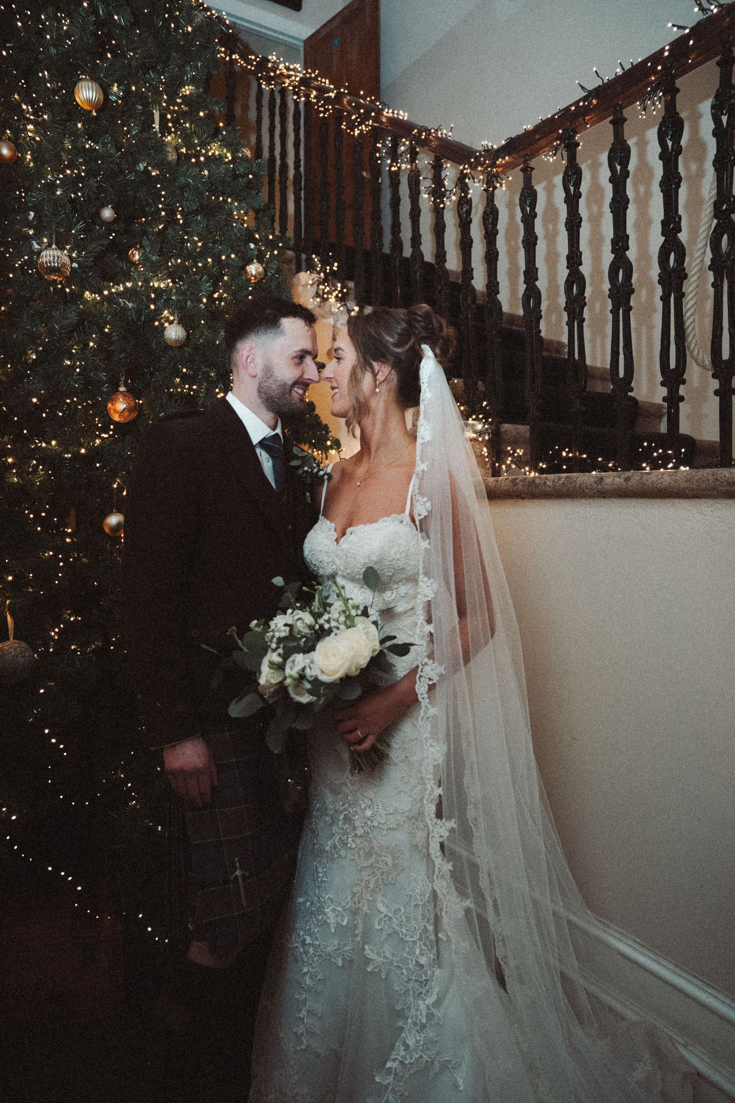 Intimate wedding moment captured by decorated Christmas tree and staircase with twinkling lights.