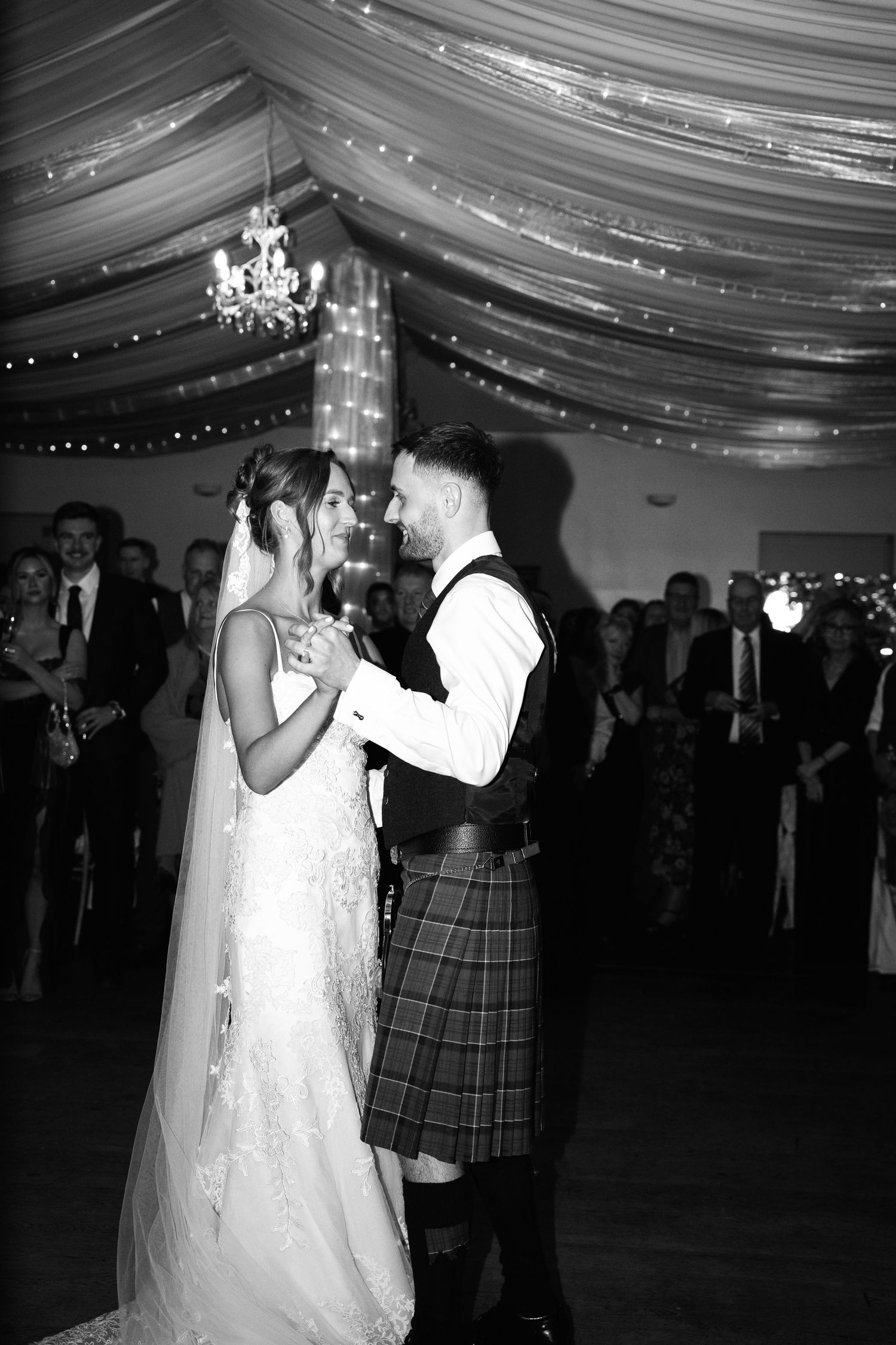 Newlyweds share an intimate dance moment under a beautifully lit tent ceiling.