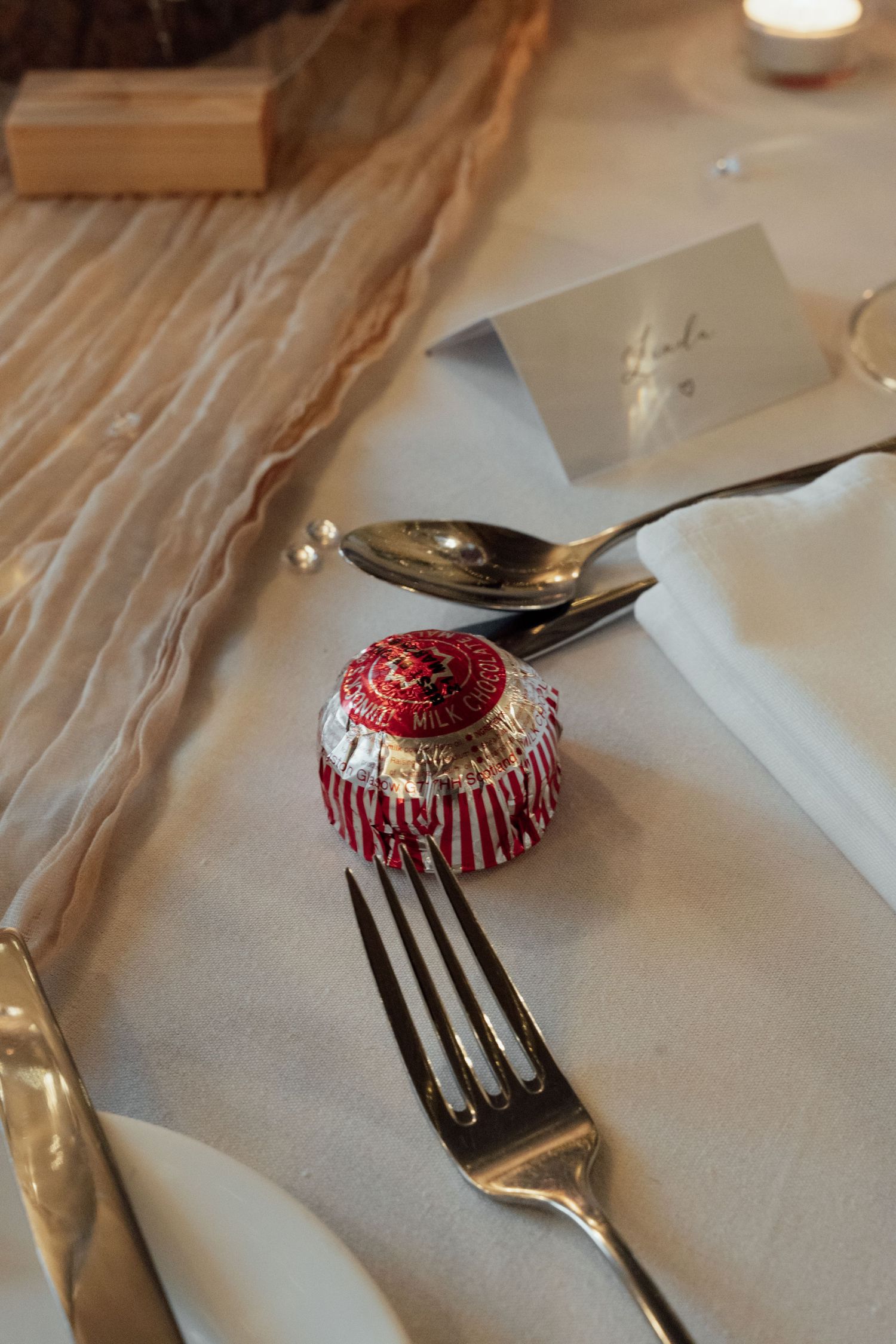 Close-up of decorative red favor or ornament with silverware on white tablecloth.