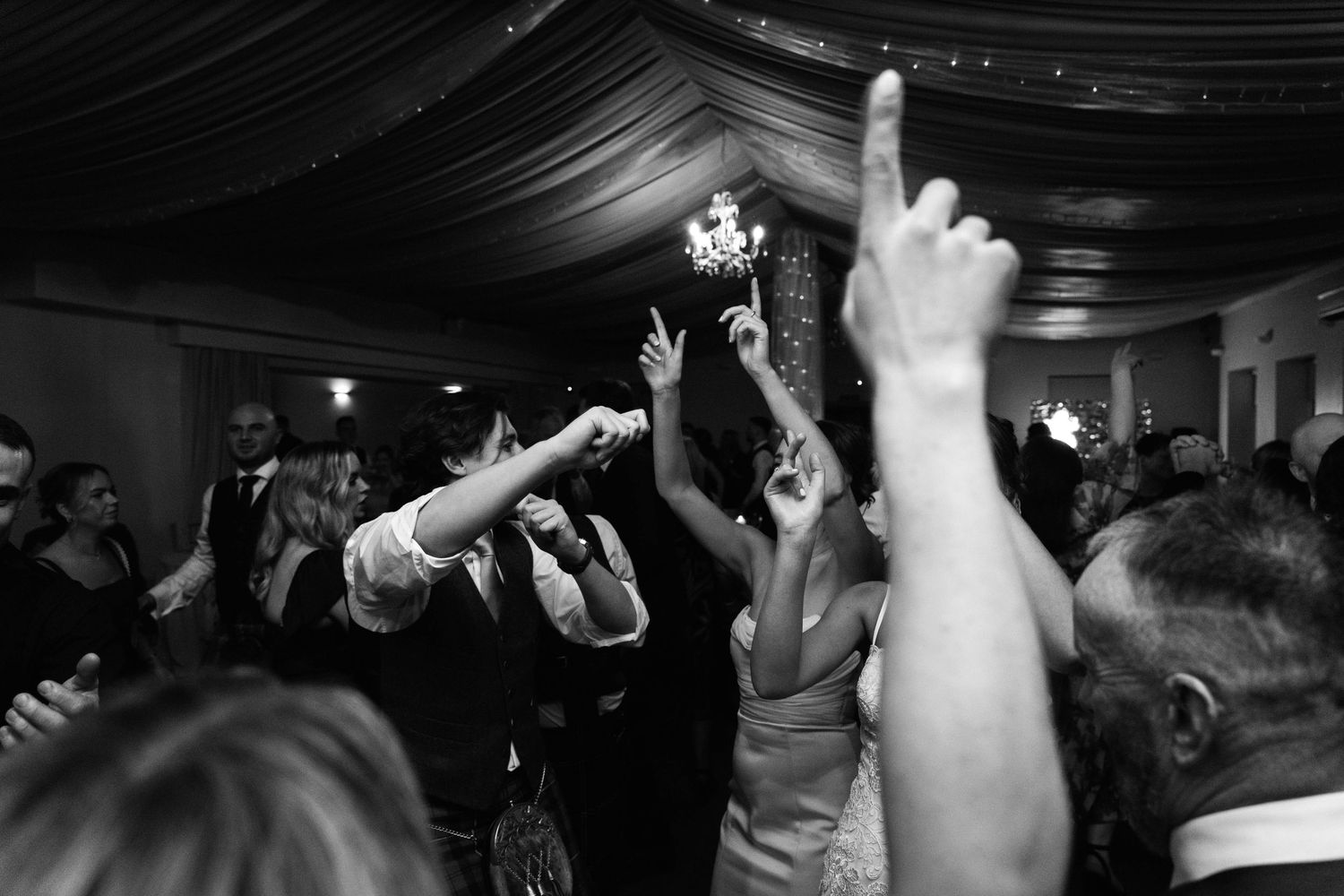 Silhouettes of wedding guests dancing with raised hands under dramatic lighting.