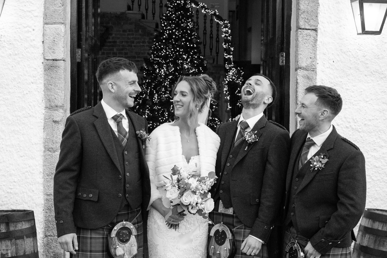 Black and white photo of wedding group laughing together in front of decorated doorway.