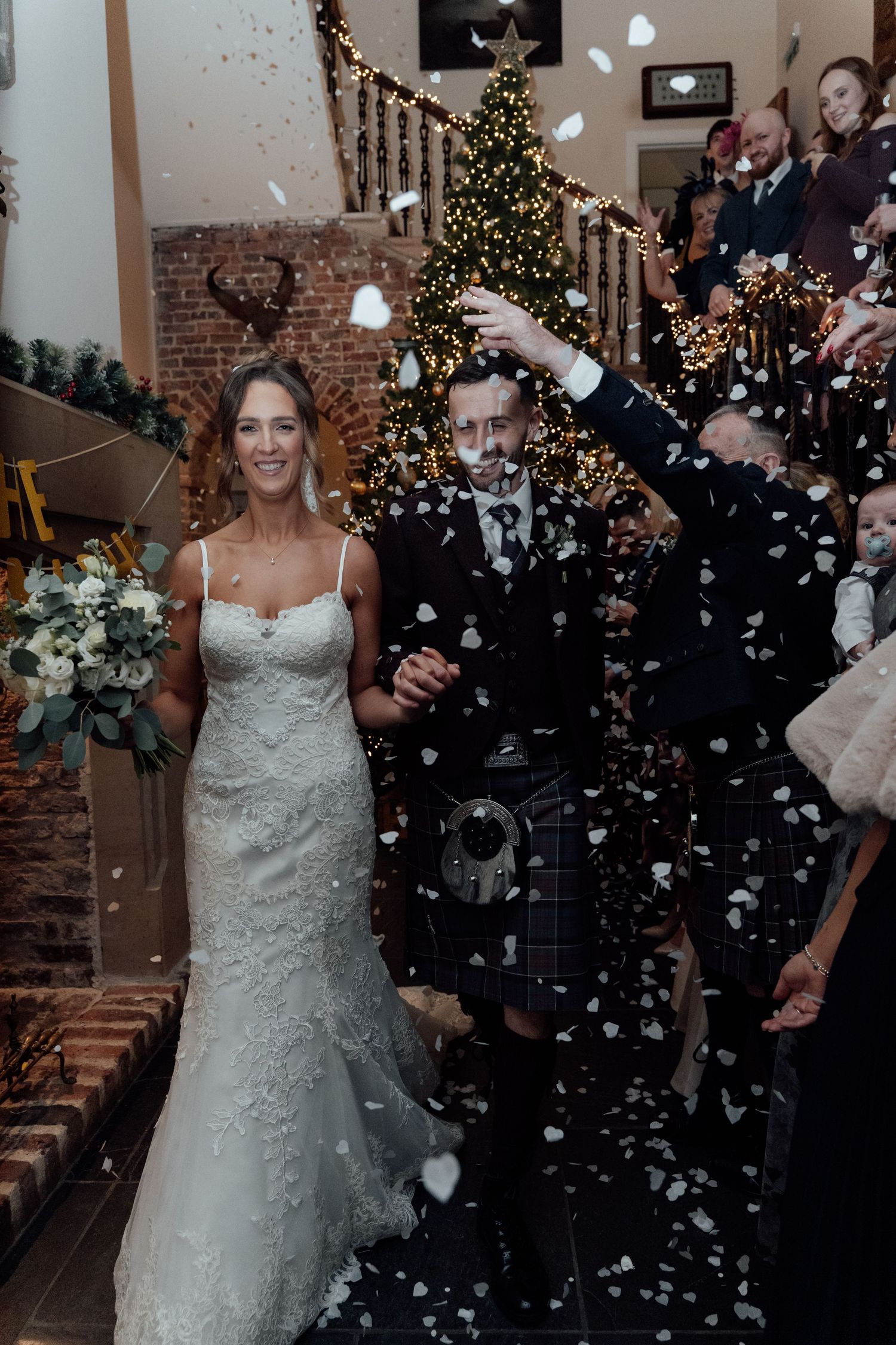 Joyful winter wedding celebration with falling confetti and Christmas tree in background.