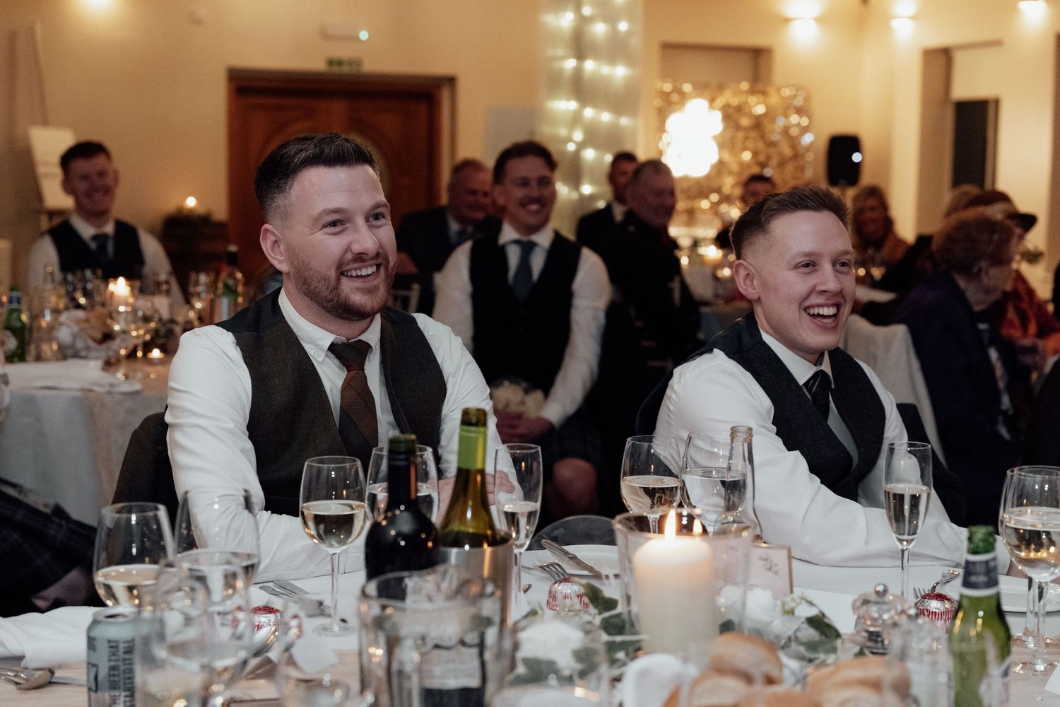 Wedding reception guests enjoying dinner and drinks at elegantly decorated tables with twinkling lights.