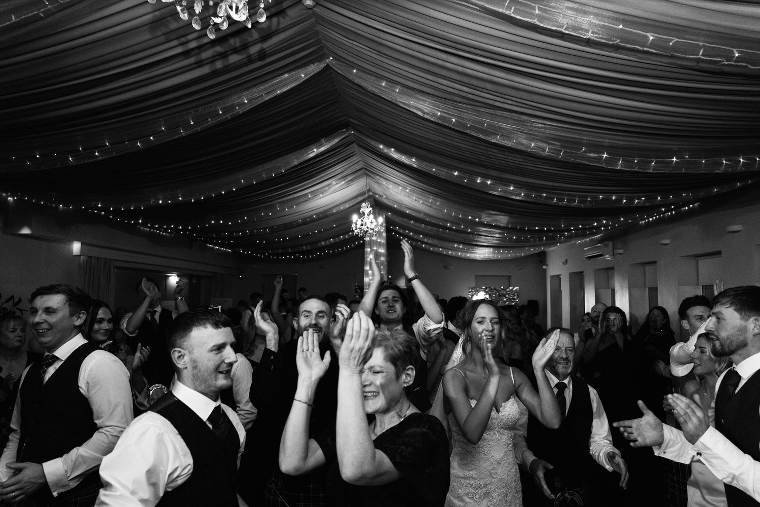 Wedding celebration with guests dancing under fabric draped ceiling with string lights.