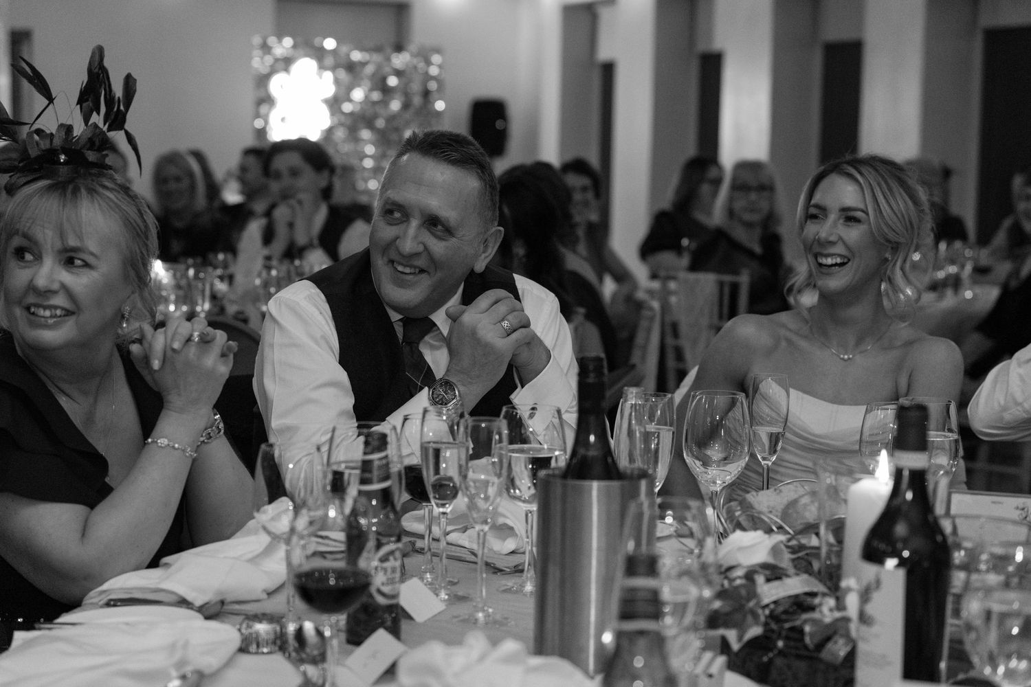 Black and white candid shot of wedding guests enjoying speeches during reception dinner.
