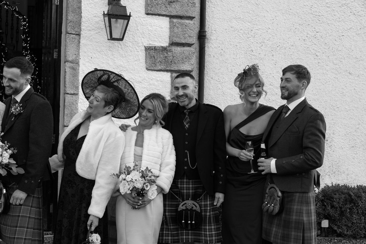 Wedding party interacting casually outside historic stone building entrance.