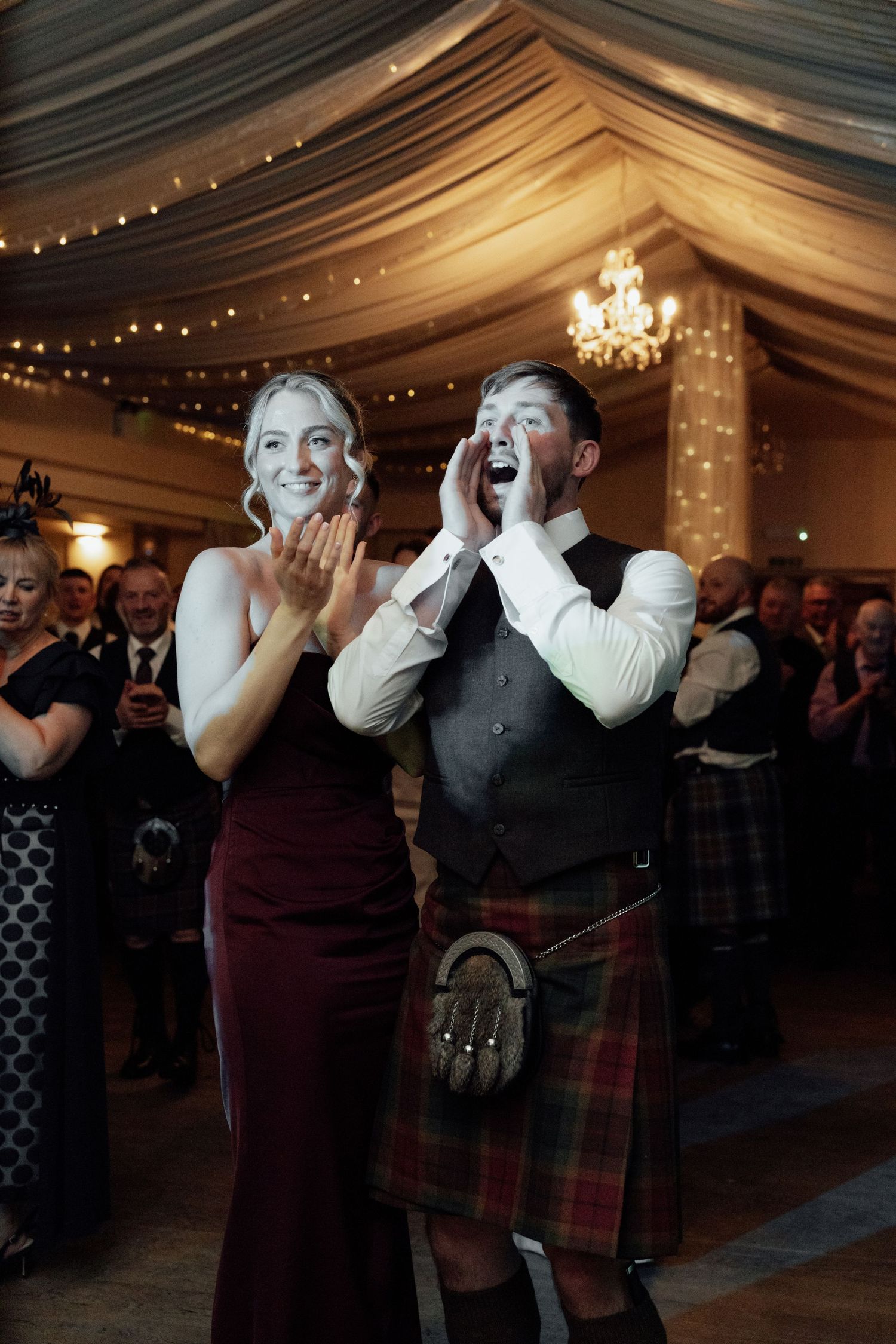 Wedding guests in traditional Scottish kilts celebrating enthusiastically on the dance floor.