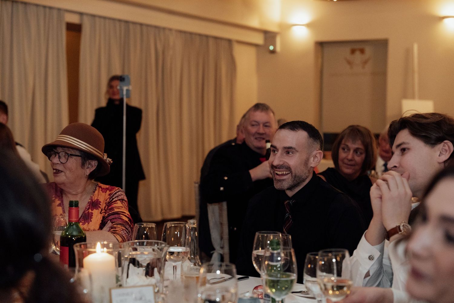 Wedding celebration captured in warm lighting with guests seated at formal dining tables.