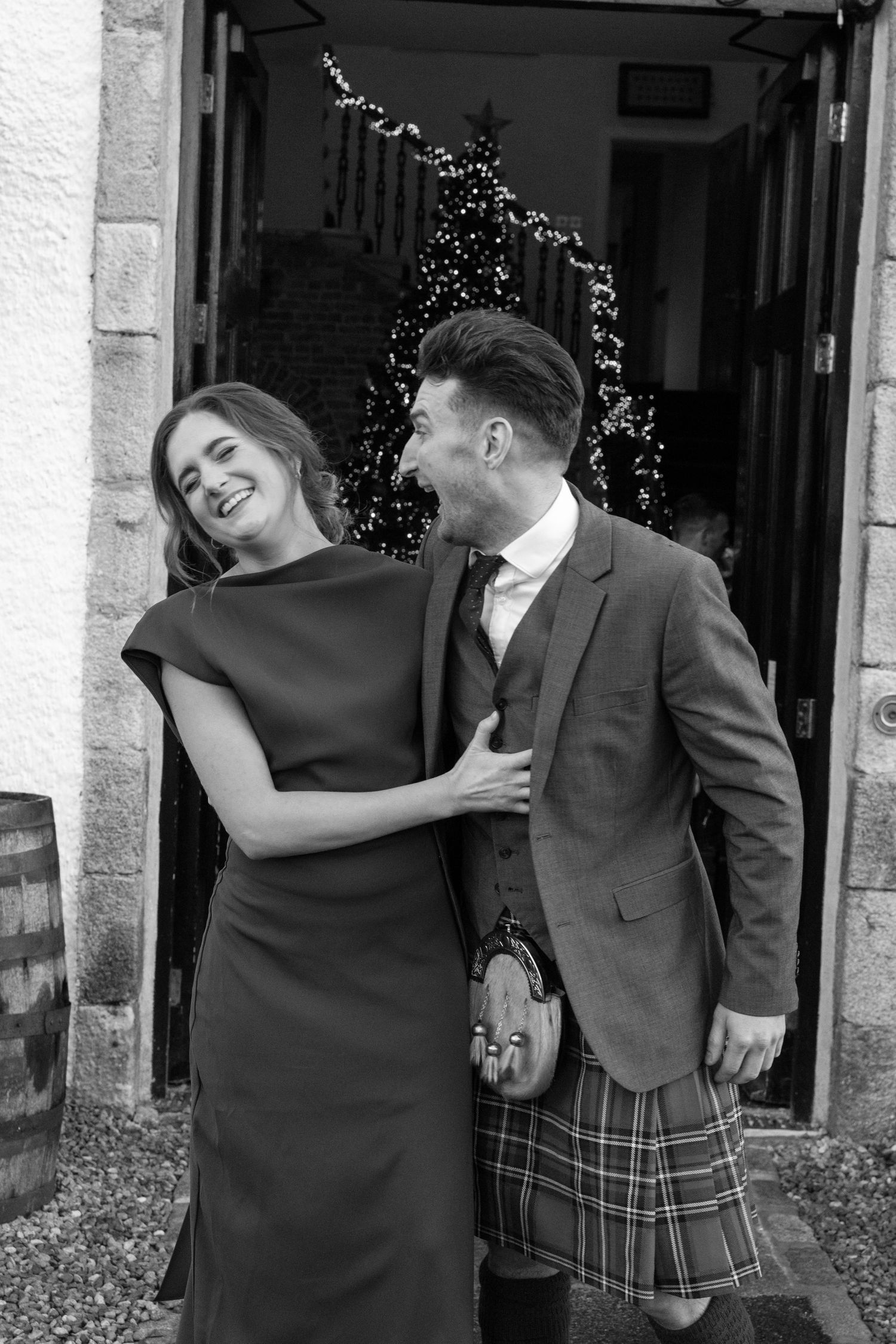 Black and white image of a couple sharing a joyful moment in front of fairy lights.