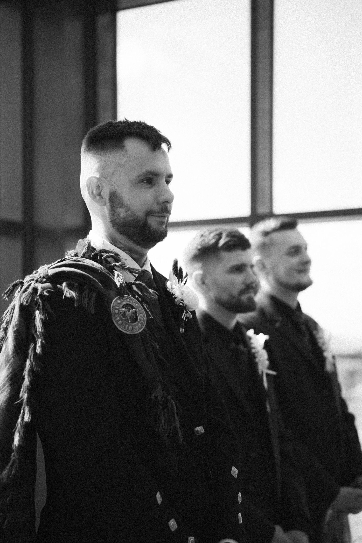 Groom in traditional Scottish Highland dress with sporran stands with groomsmen in black and white photo.