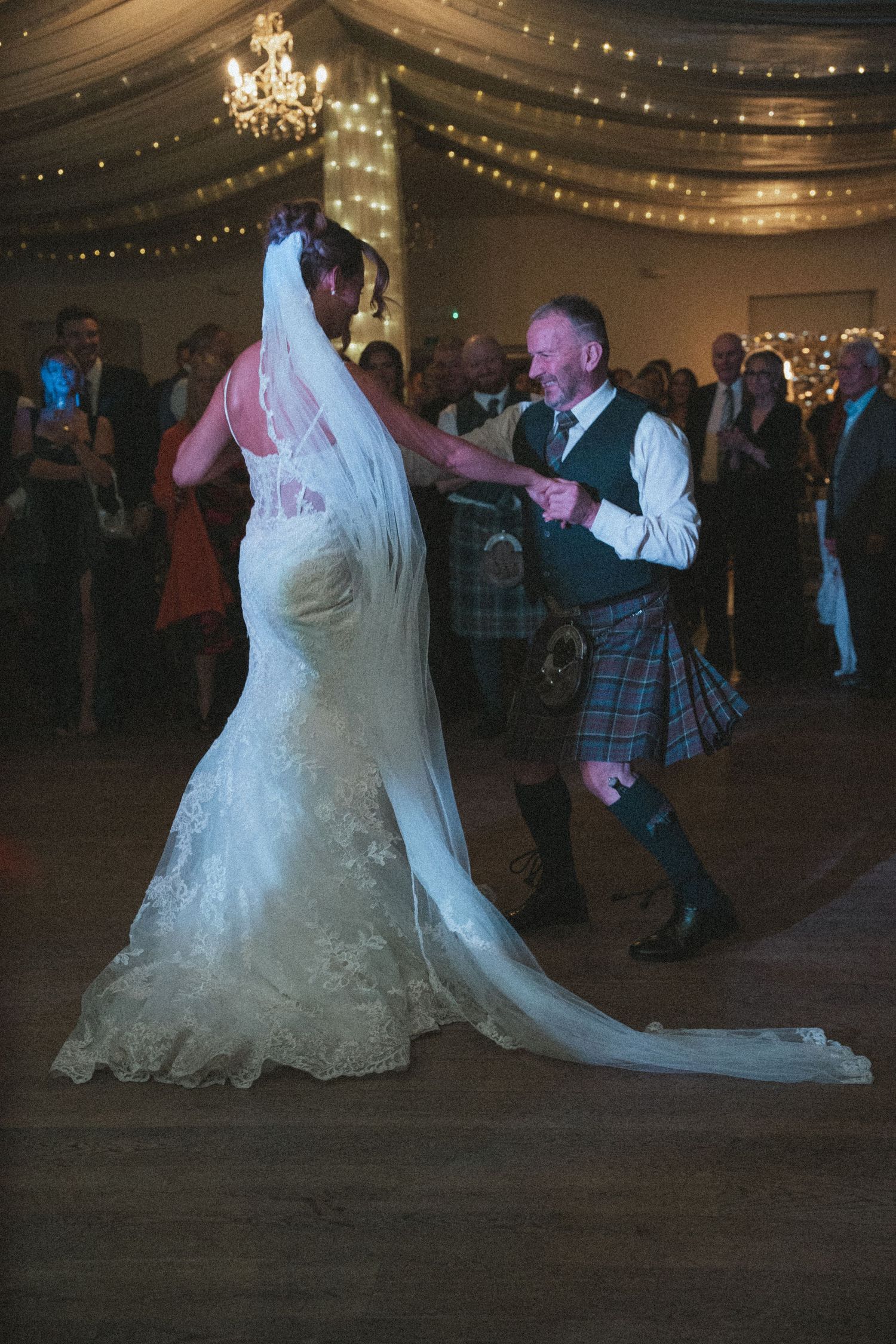 A bride in a flowing white gown dances with guests at an evening reception.