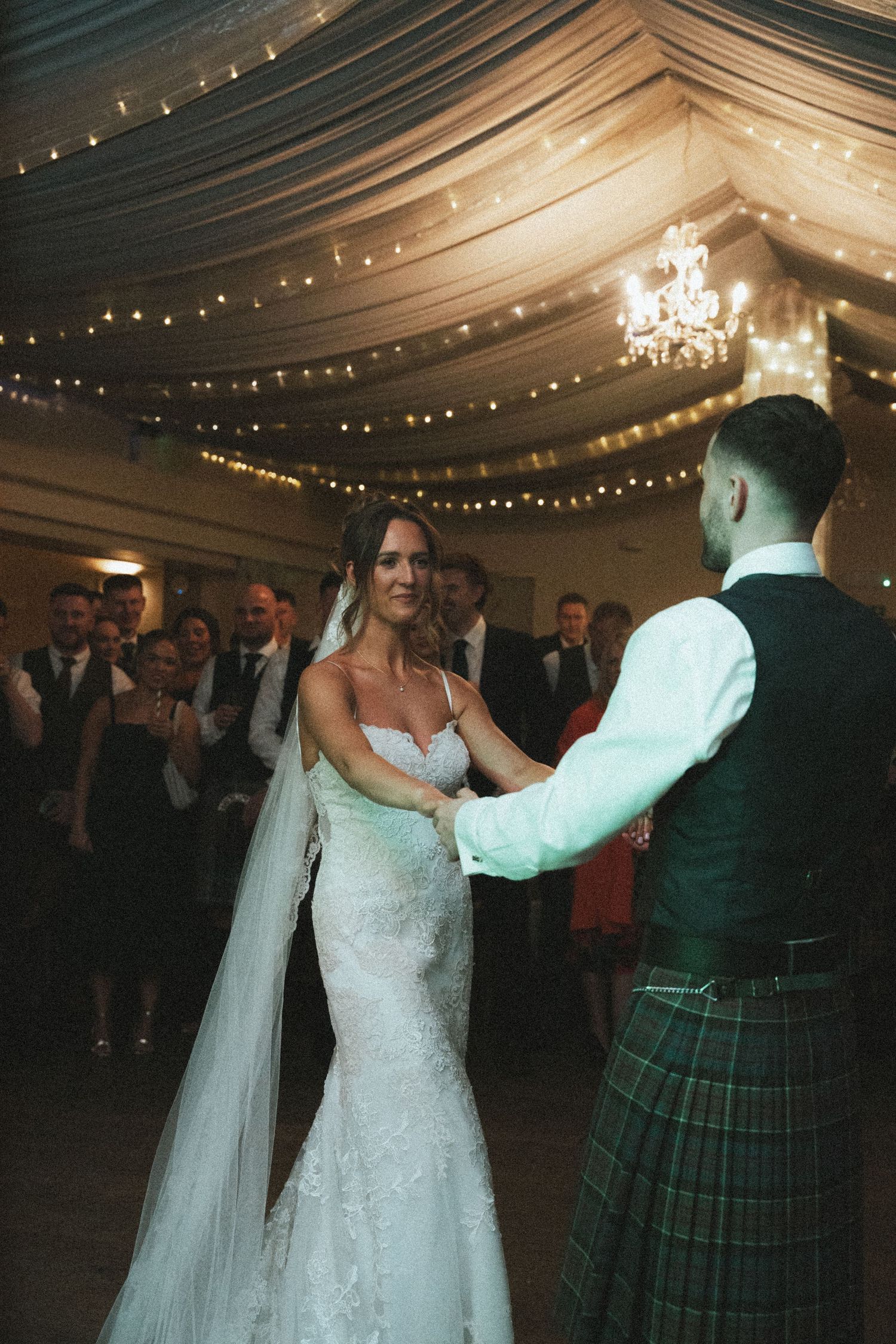 Couple sharing their first dance in a tent venue with romantic lighting and Scottish attire.