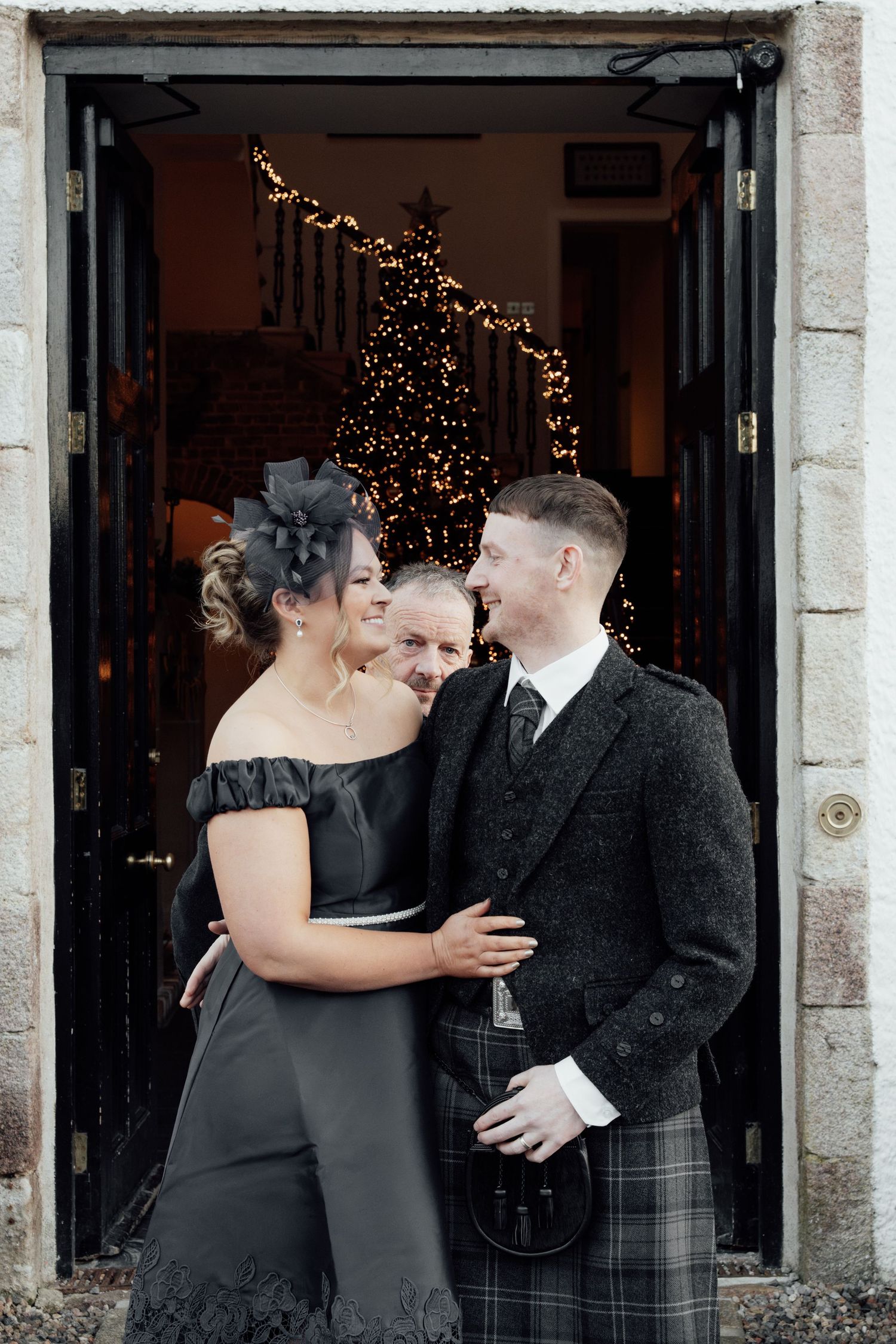 Wedding party members share candid moments outside venue entrance with stone details.