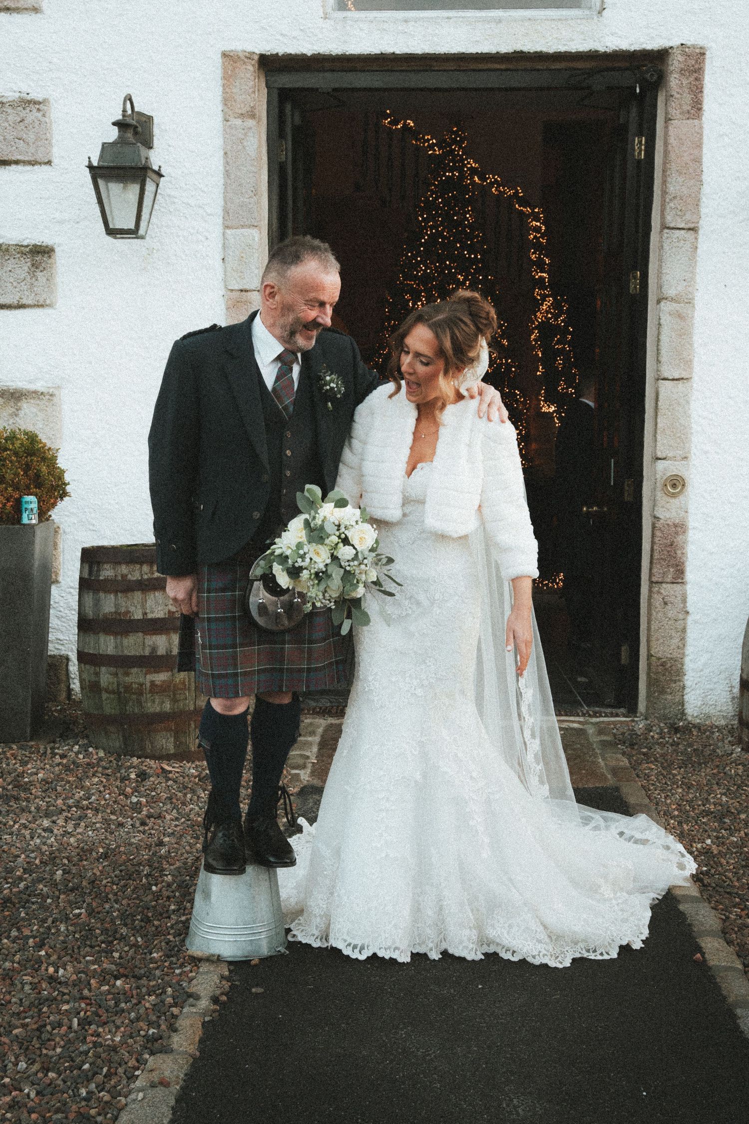 A wedding couple poses outside a white building with fairy lights and rustic decor.