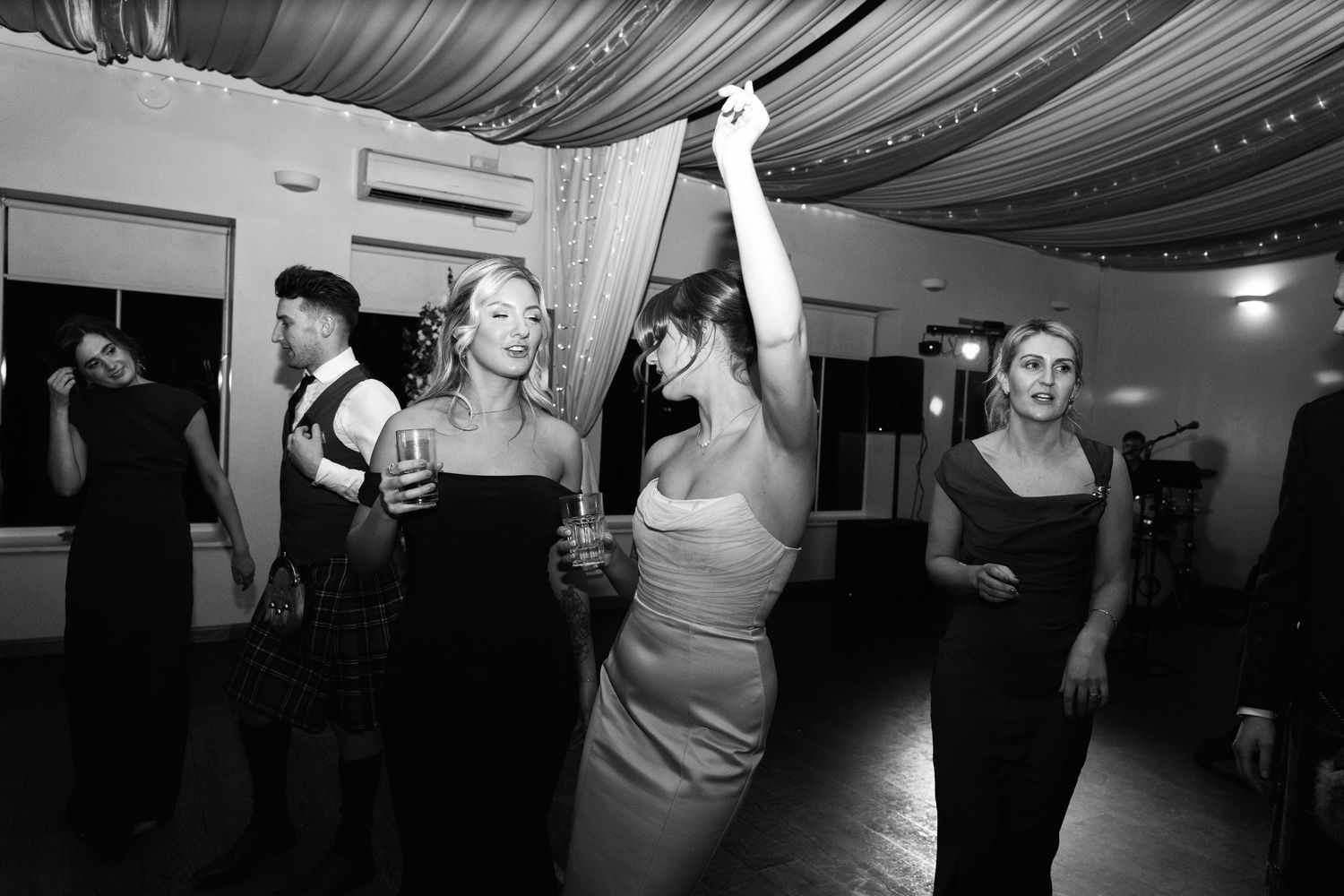 Black and white photo of wedding reception dancing under dramatic ceiling drapes.