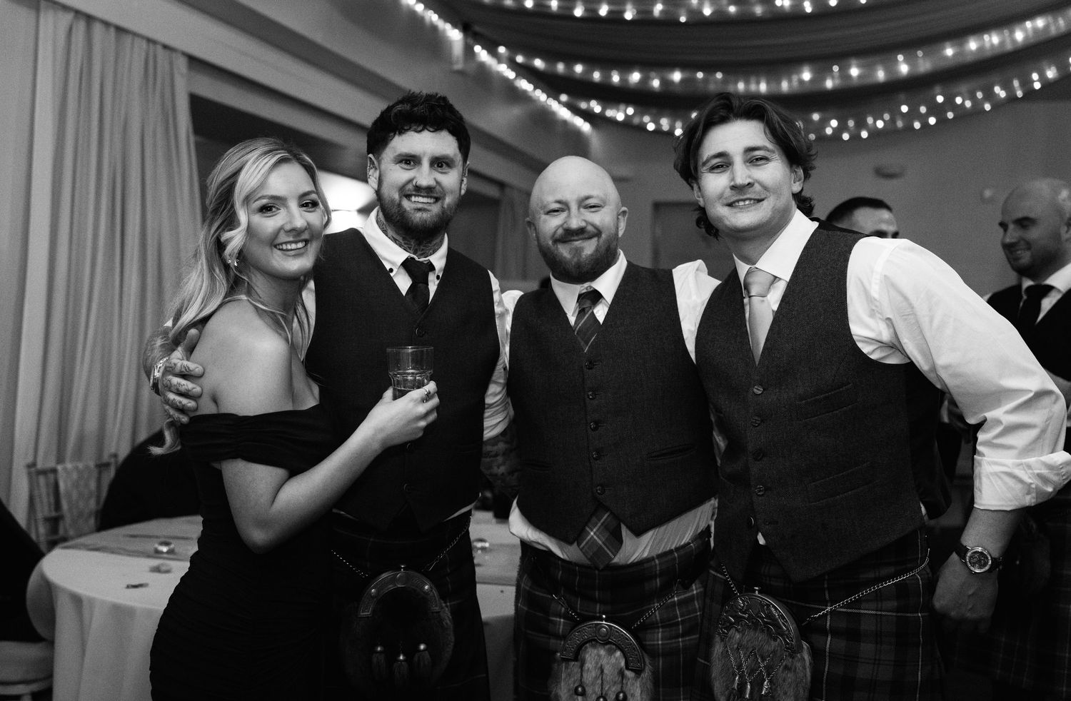 Guests celebrate at a wedding reception with string lights decorating the ceiling.
