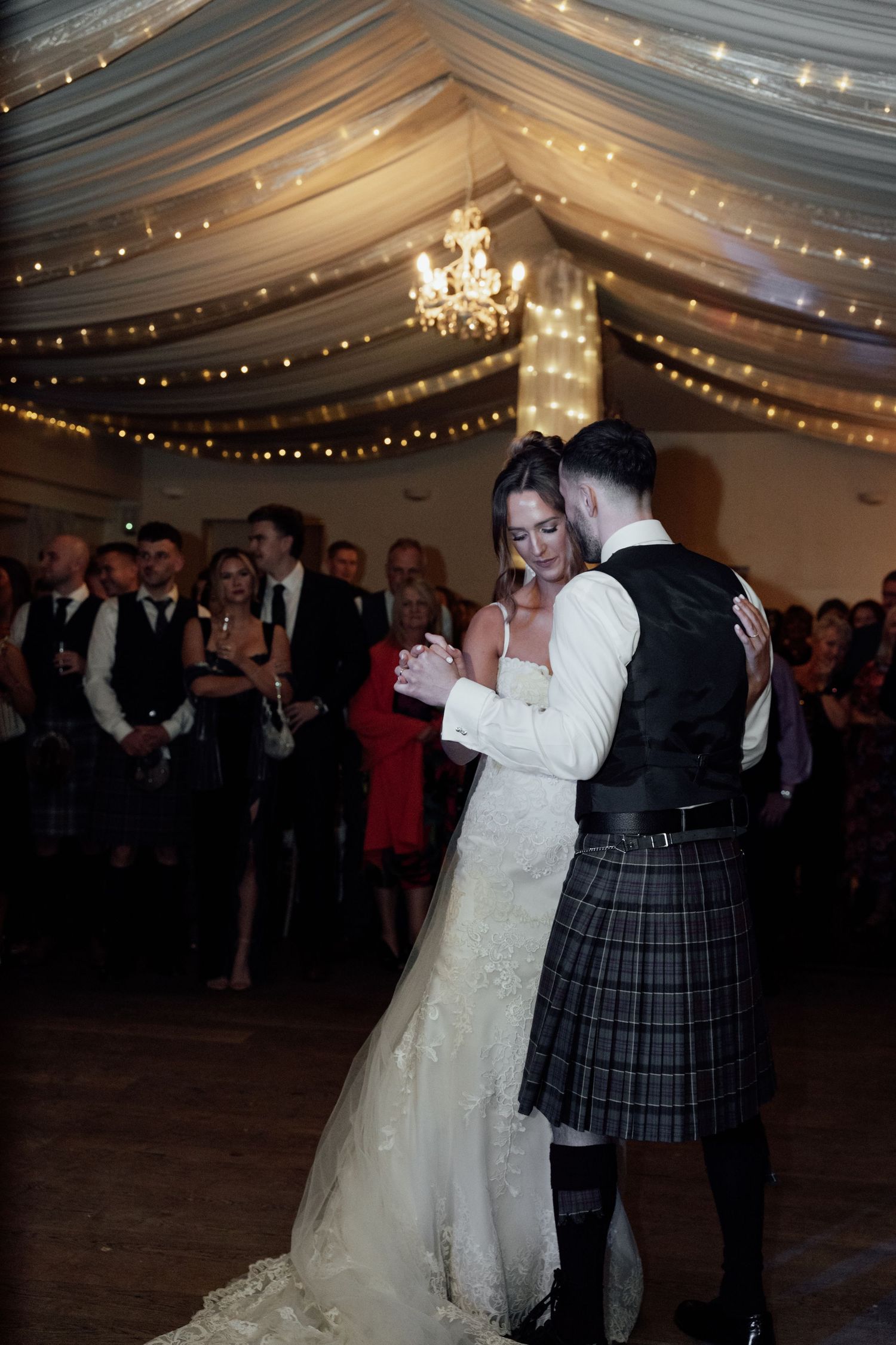 Wedding couple dancing in a decorated marquee with fairy lights and white fabric draping.
