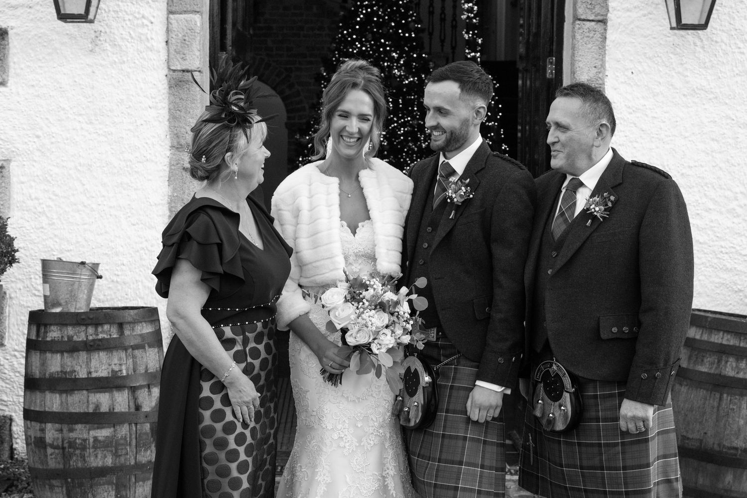 Wedding group photo with mix of kilts and formal wear outside venue entrance.