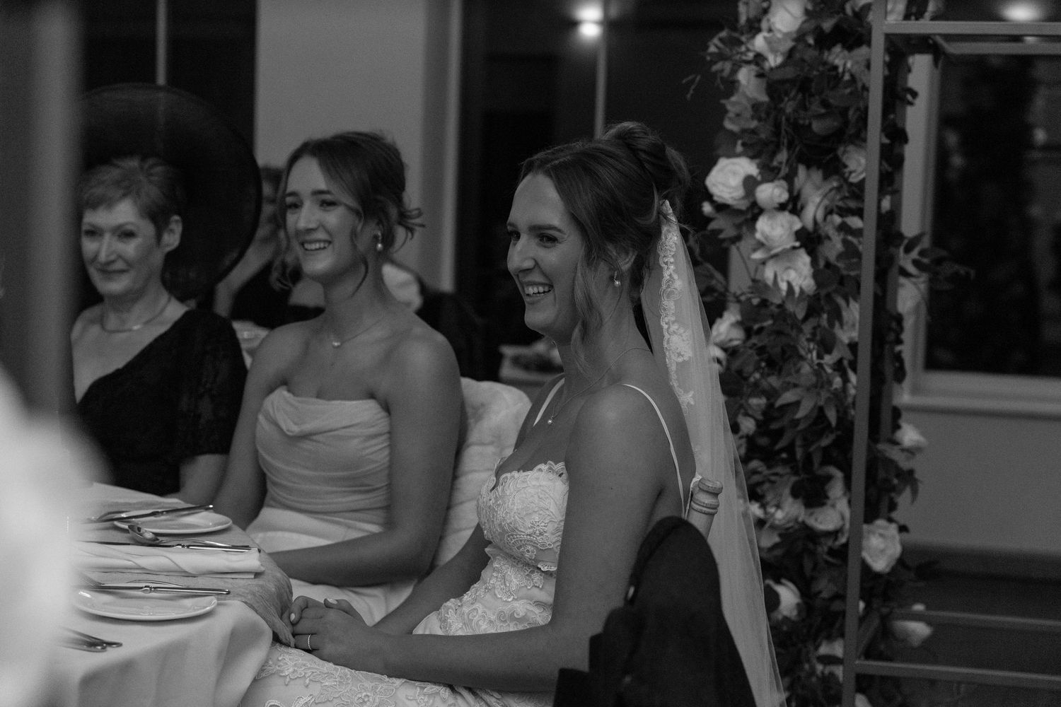Wedding guests share joyful moments at reception tables decorated with white floral arrangements.