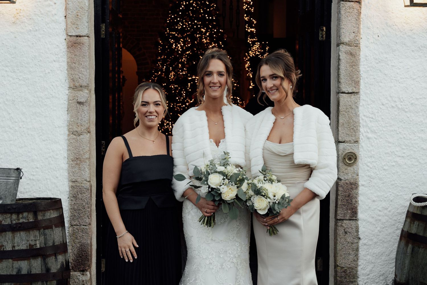 Group photo of wedding party in black and white dresses holding bouquets against white stone wall.