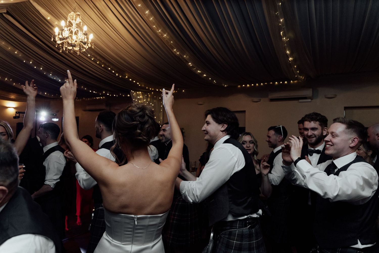 Guests enjoying a lively celebration on the dance floor with Scottish kilts visible in the crowd.