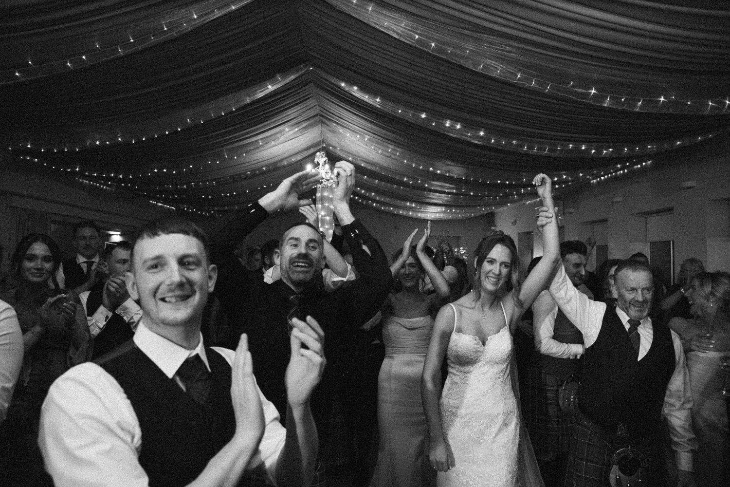 Wedding celebration with people dancing under dramatic black ceiling drapes and twinkle lights.