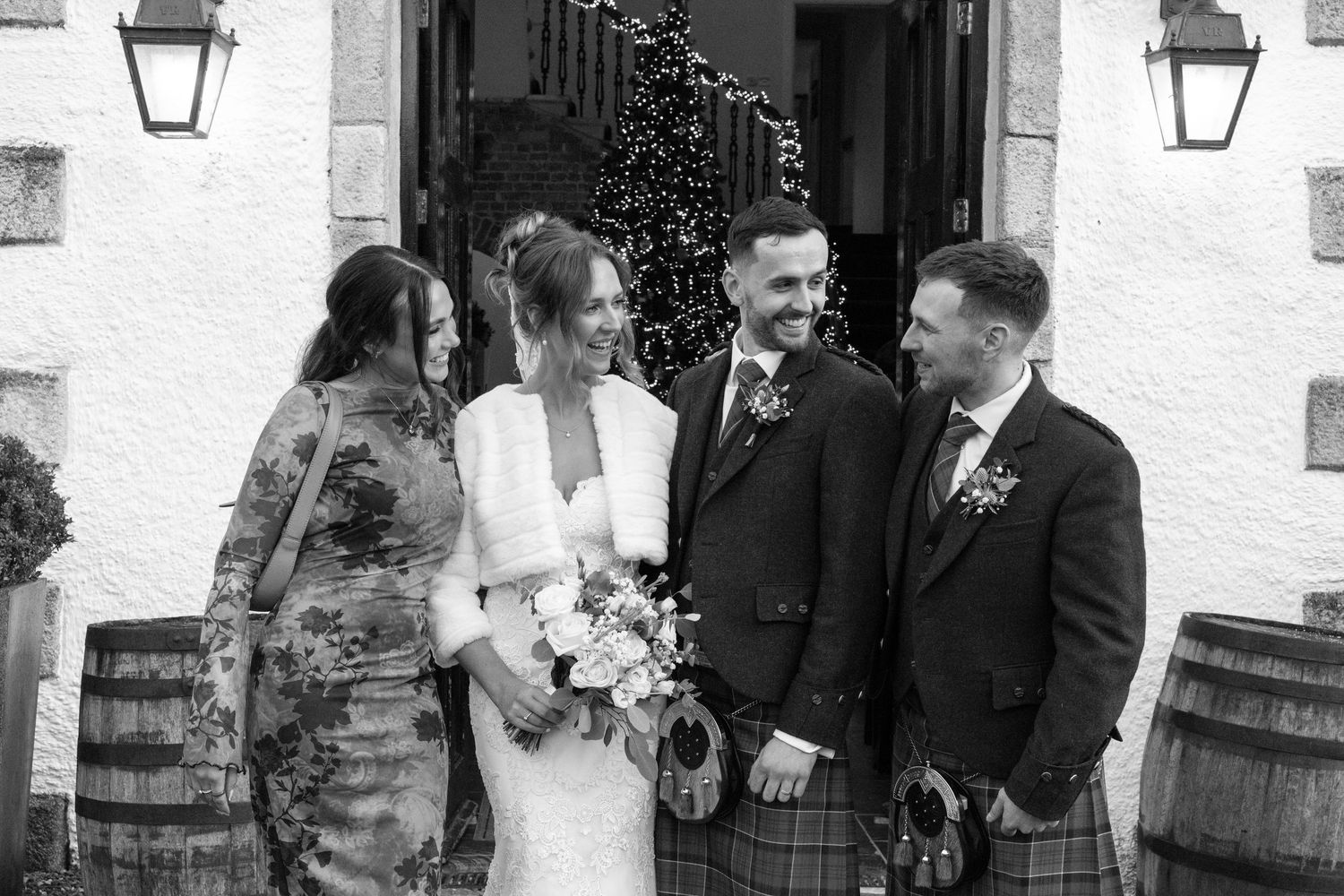 Wedding party members smile while standing outside venue entrance with lanterns.