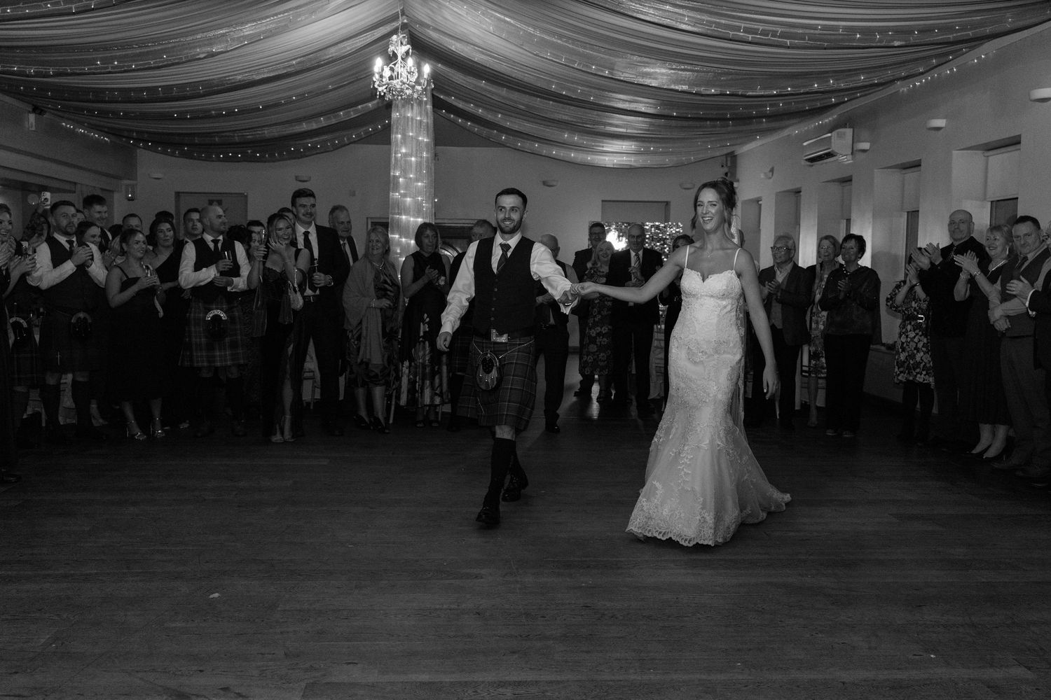 Wide shot of a decorated wedding reception hall with draped ceiling and dancing guests.