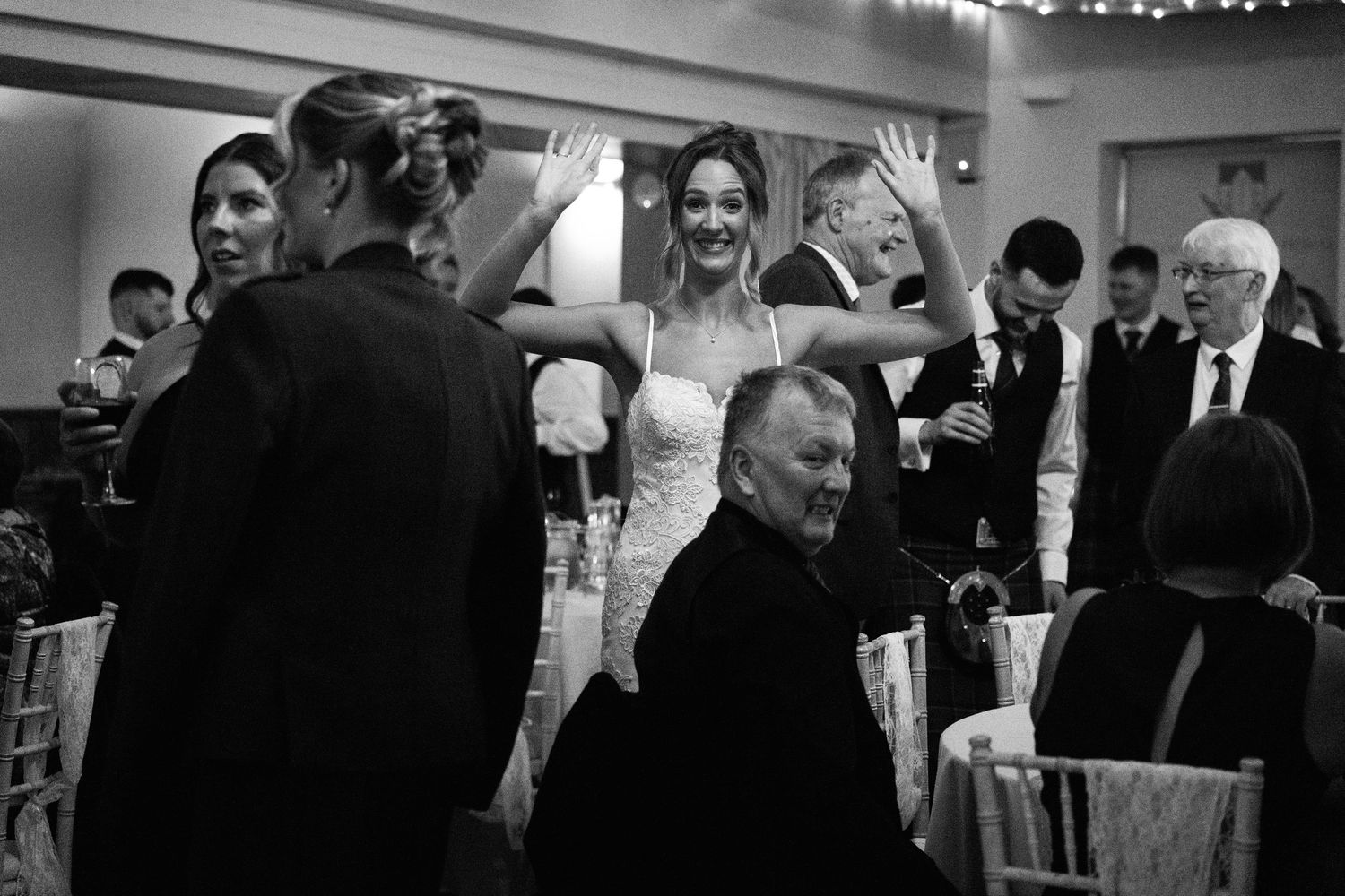 A celebratory moment at a wedding reception with guests cheering and raising hands.