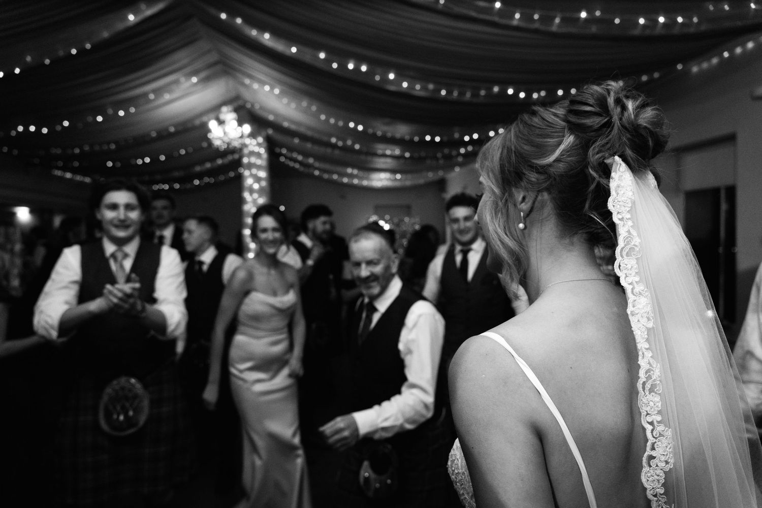 Wedding party dancing under elegant black fabric draping and twinkling lights.