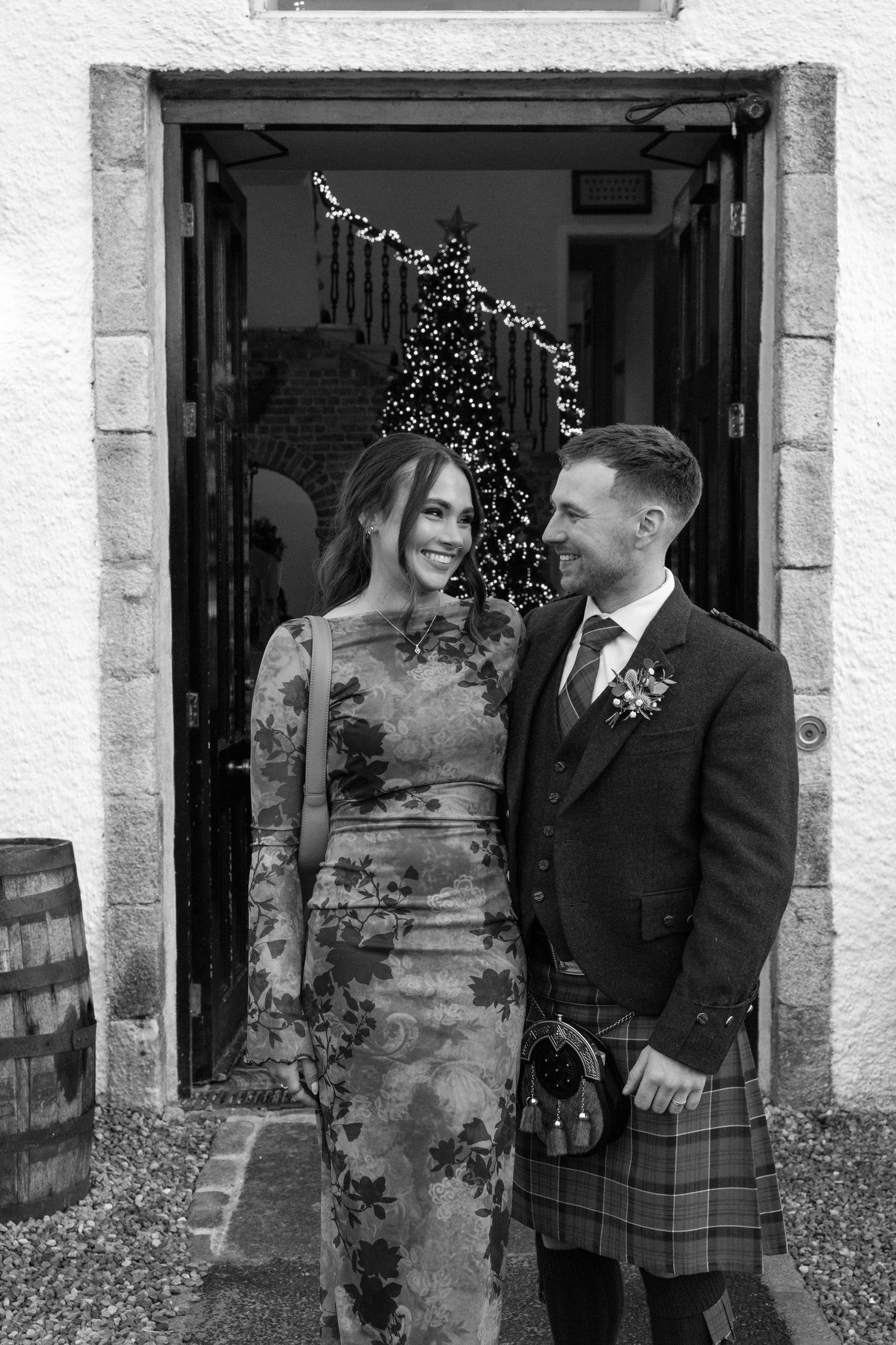 Couple shares a candid moment while posing for wedding photos outside a white stone building.