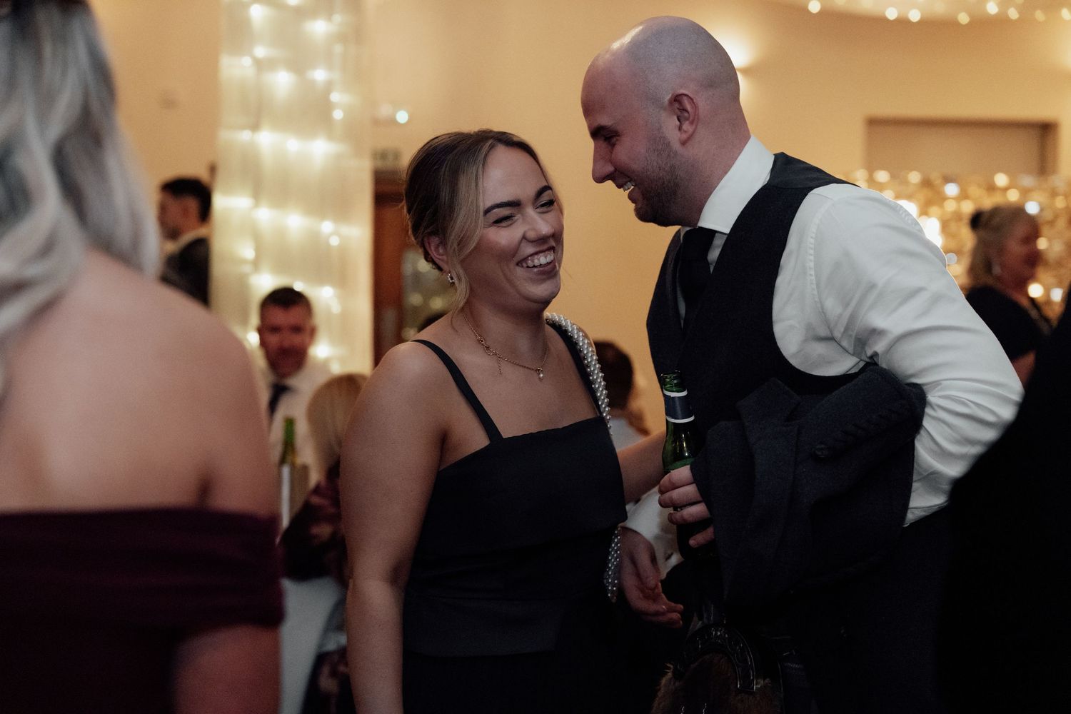 Guests share a joyful moment during a wedding reception in a warmly lit venue.