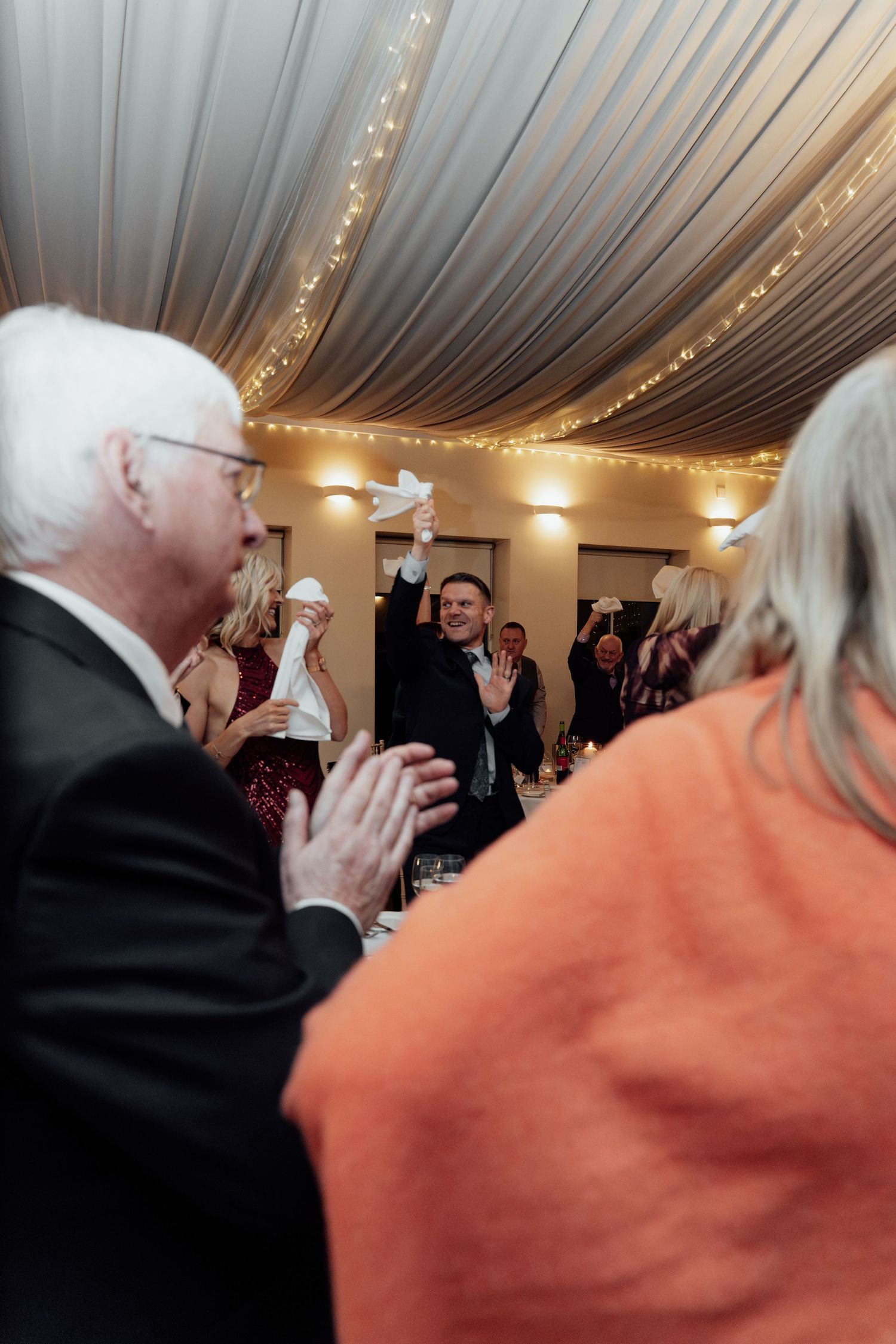 Wedding reception guests dancing under elegant draped ceiling with warm lighting.