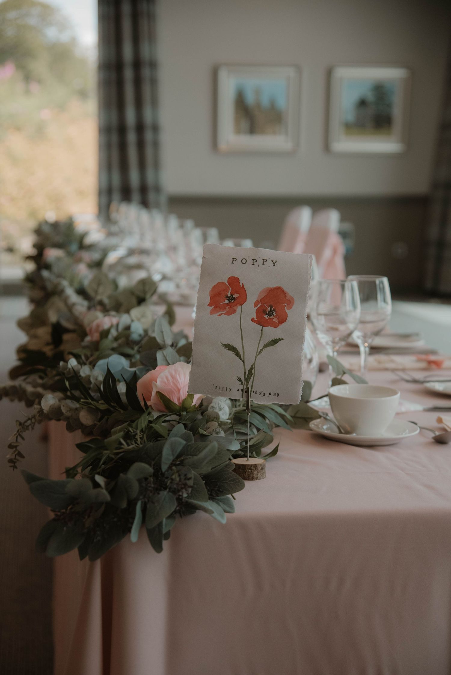 Elegant wedding reception table setting with pink flowers, eucalyptus, and delicate place cards.