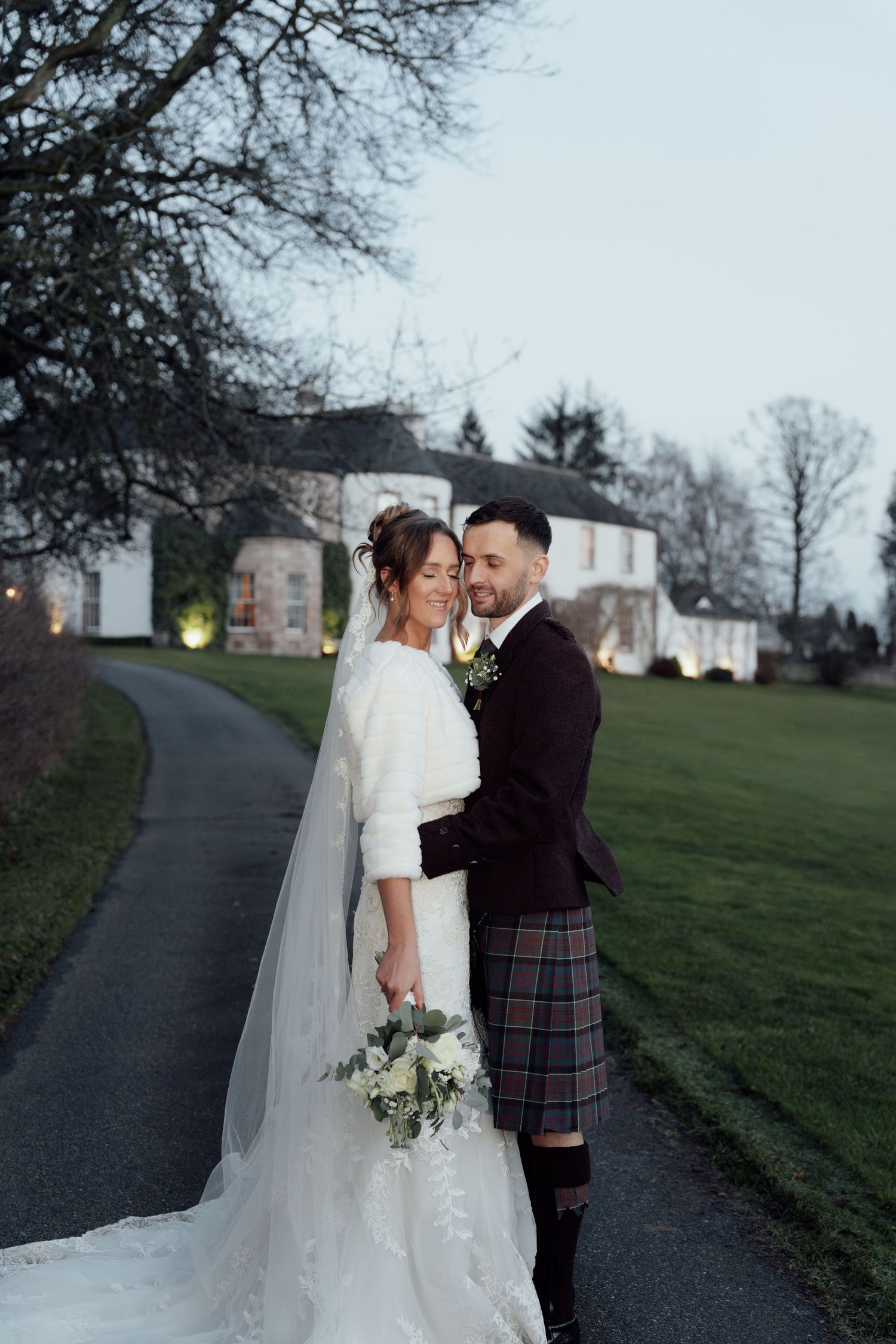 Romantic wedding couple shares an intimate moment on a path near a historic white building.