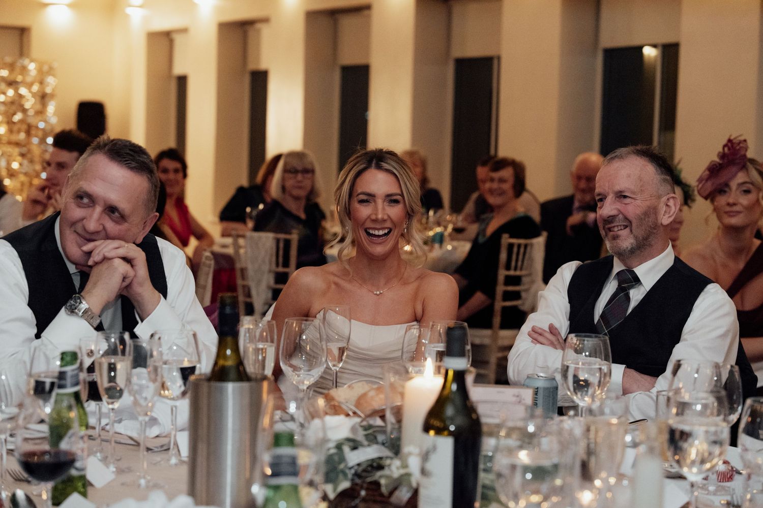 Wedding reception guests laughing during dinner at elegantly set tables with wine glasses.
