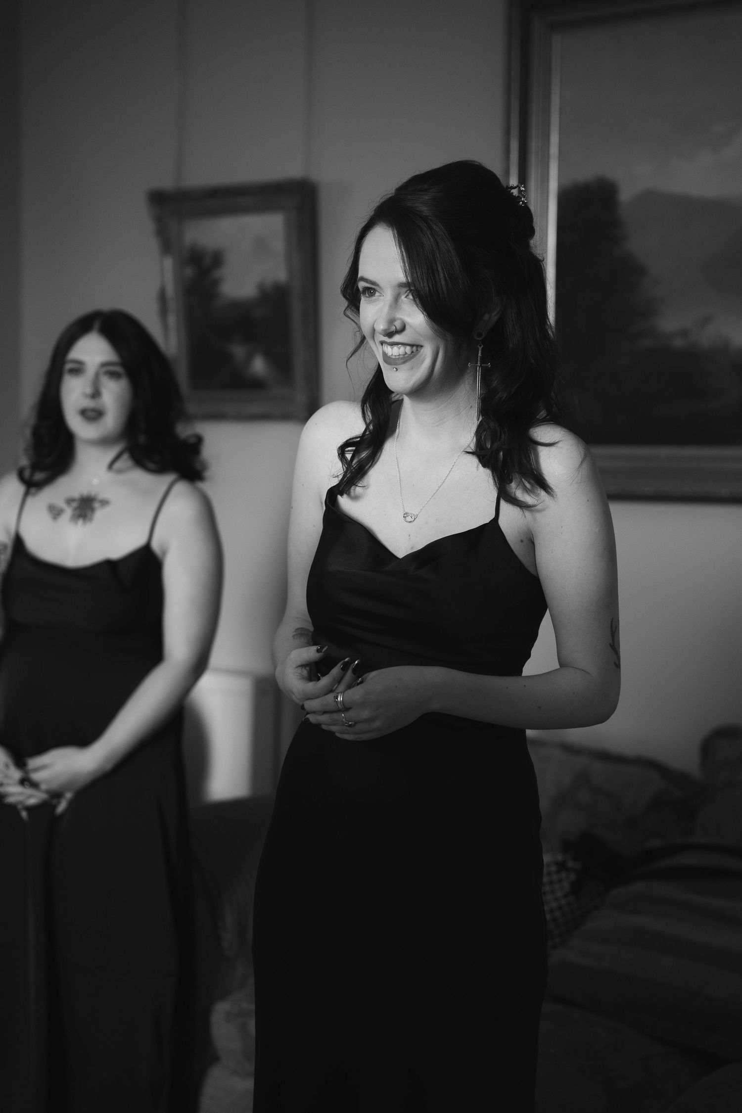 Black and white photo of two smiling bridesmaids in black dresses getting ready for a wedding.