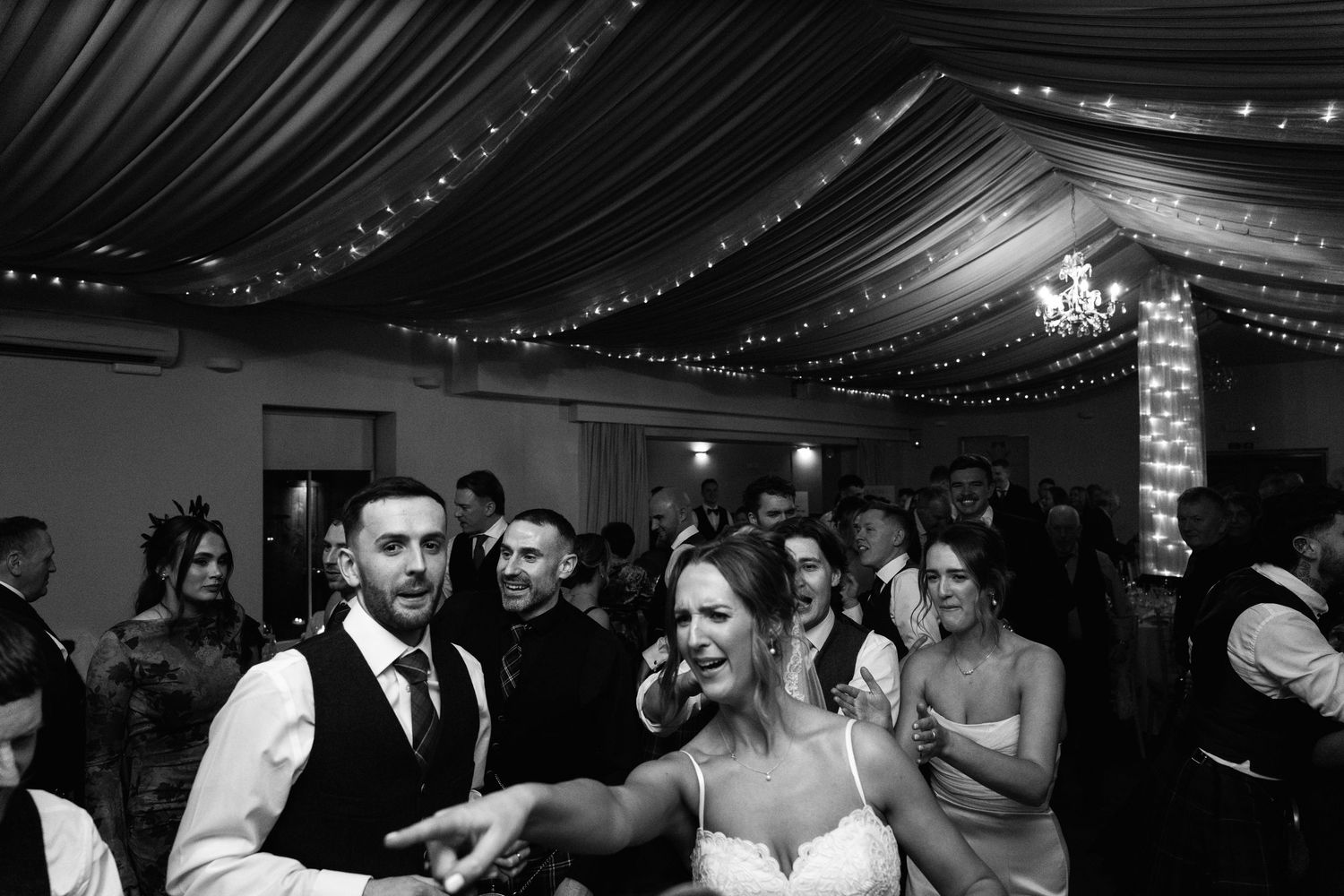Celebration on dance floor with guests dancing beneath draped fabric and string lights.
