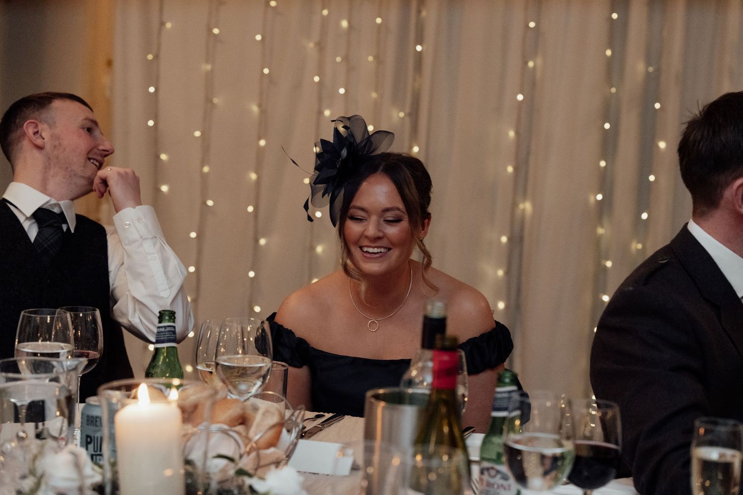 Wedding guests enjoying dinner and conversation at an elegant reception with twinkling lights and candles.