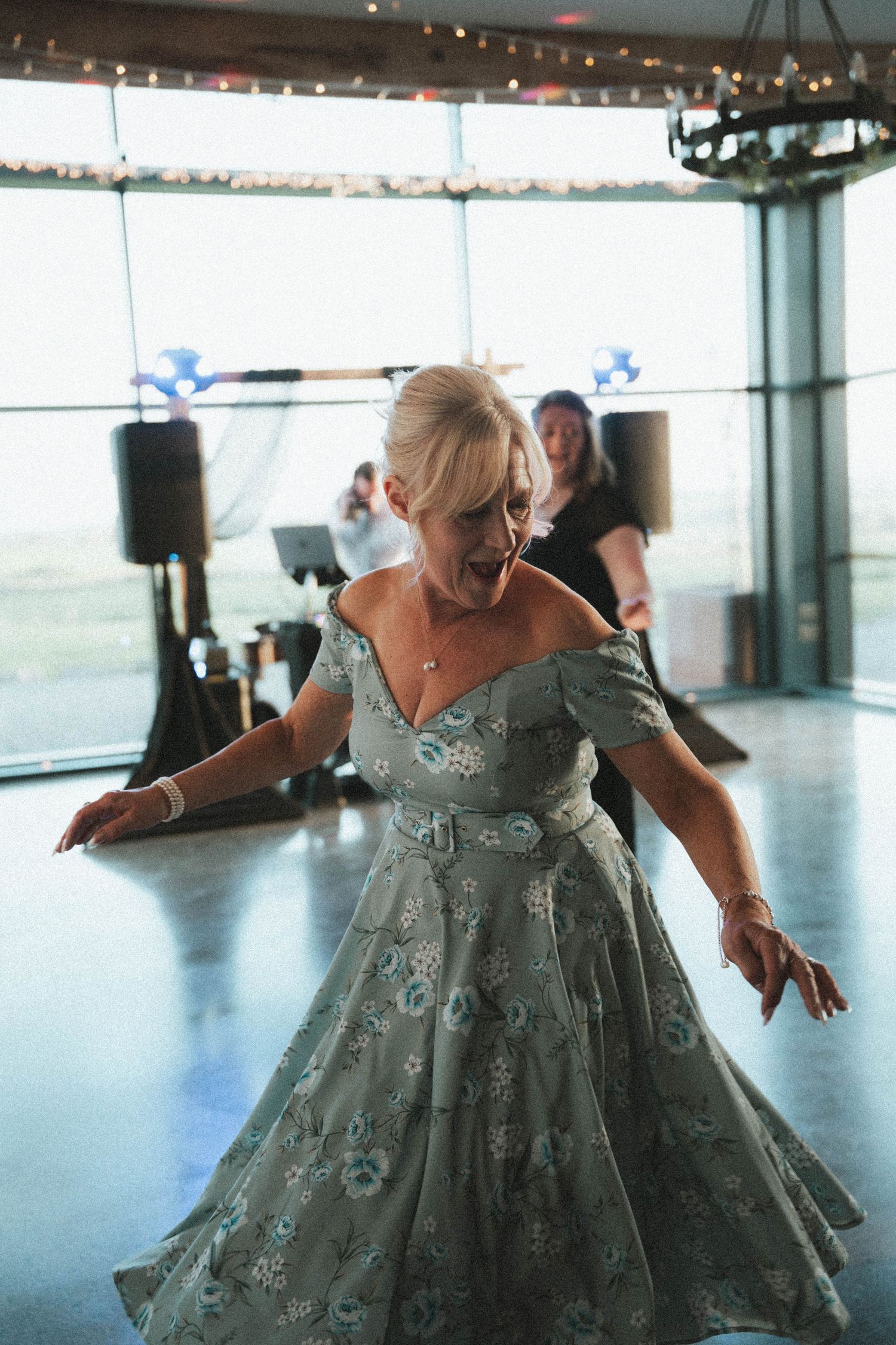 Older woman in vintage floral off-shoulder dress dancing energetically at wedding reception.