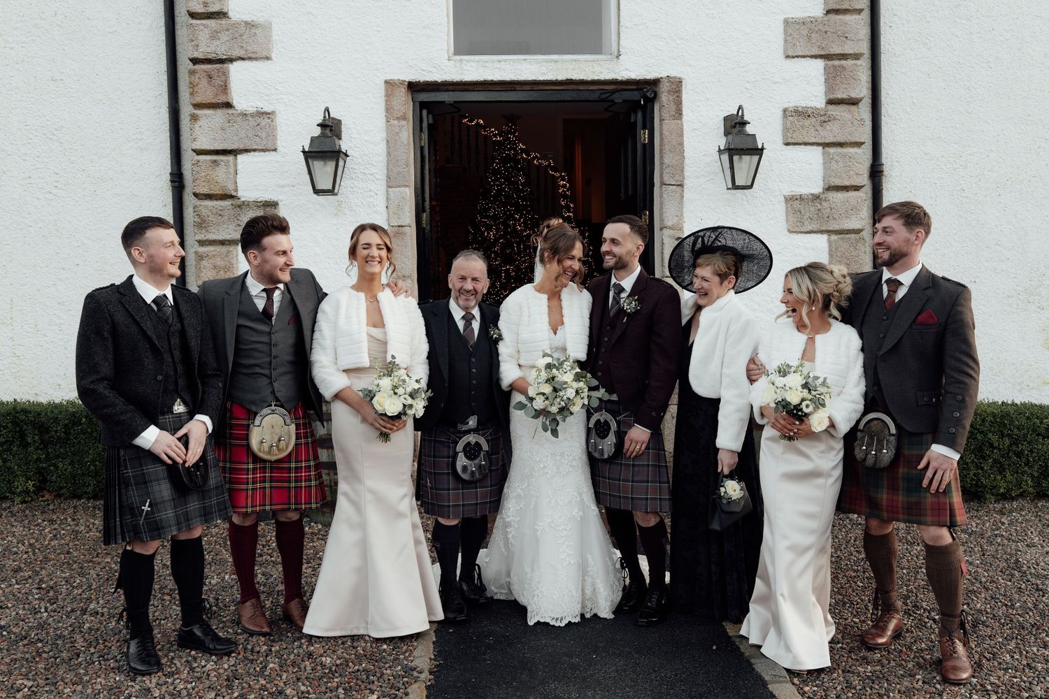 Wedding group arranged for photos outside traditional Scottish venue.