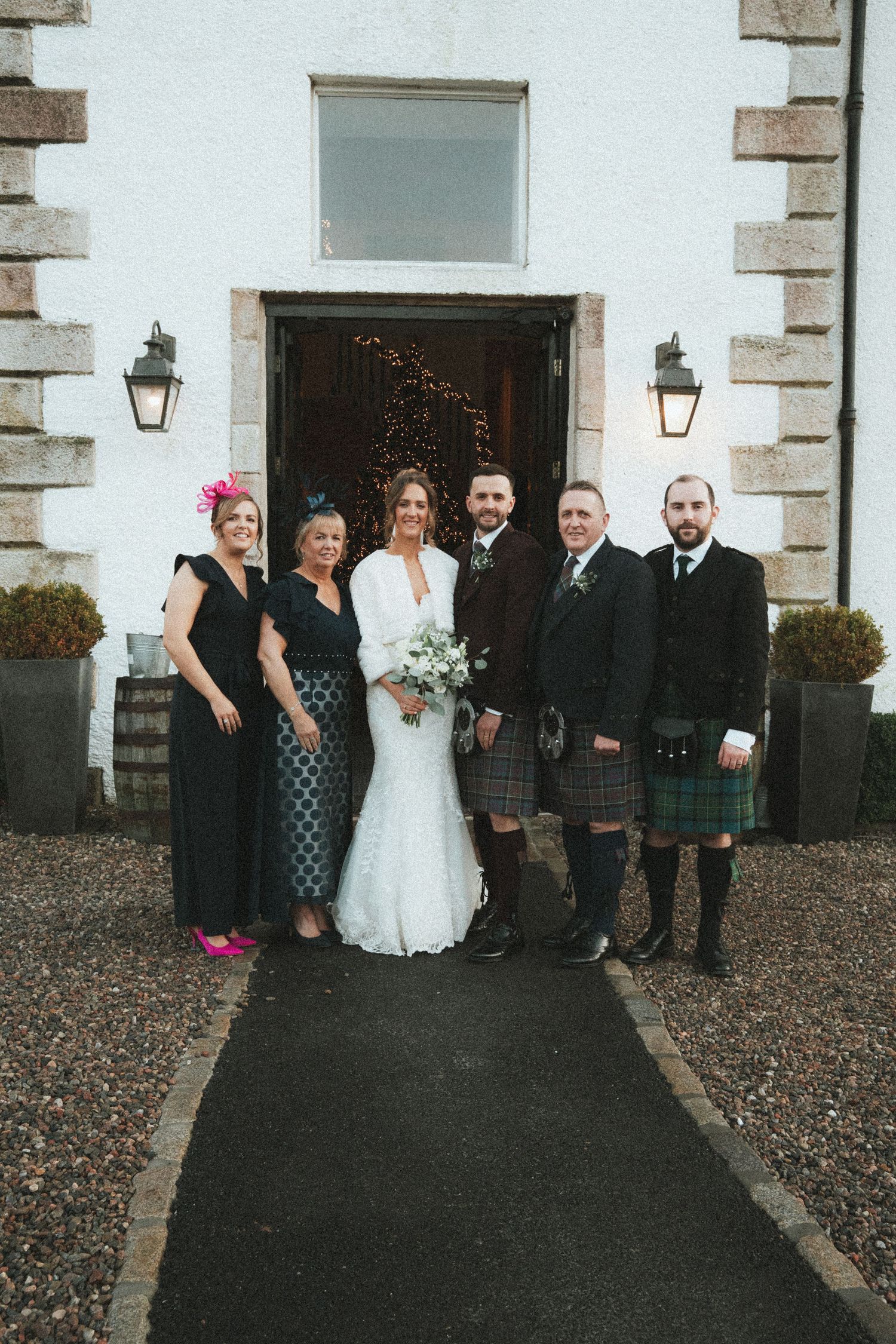 Wedding group photo outside white stone building with traditional Scottish attire.