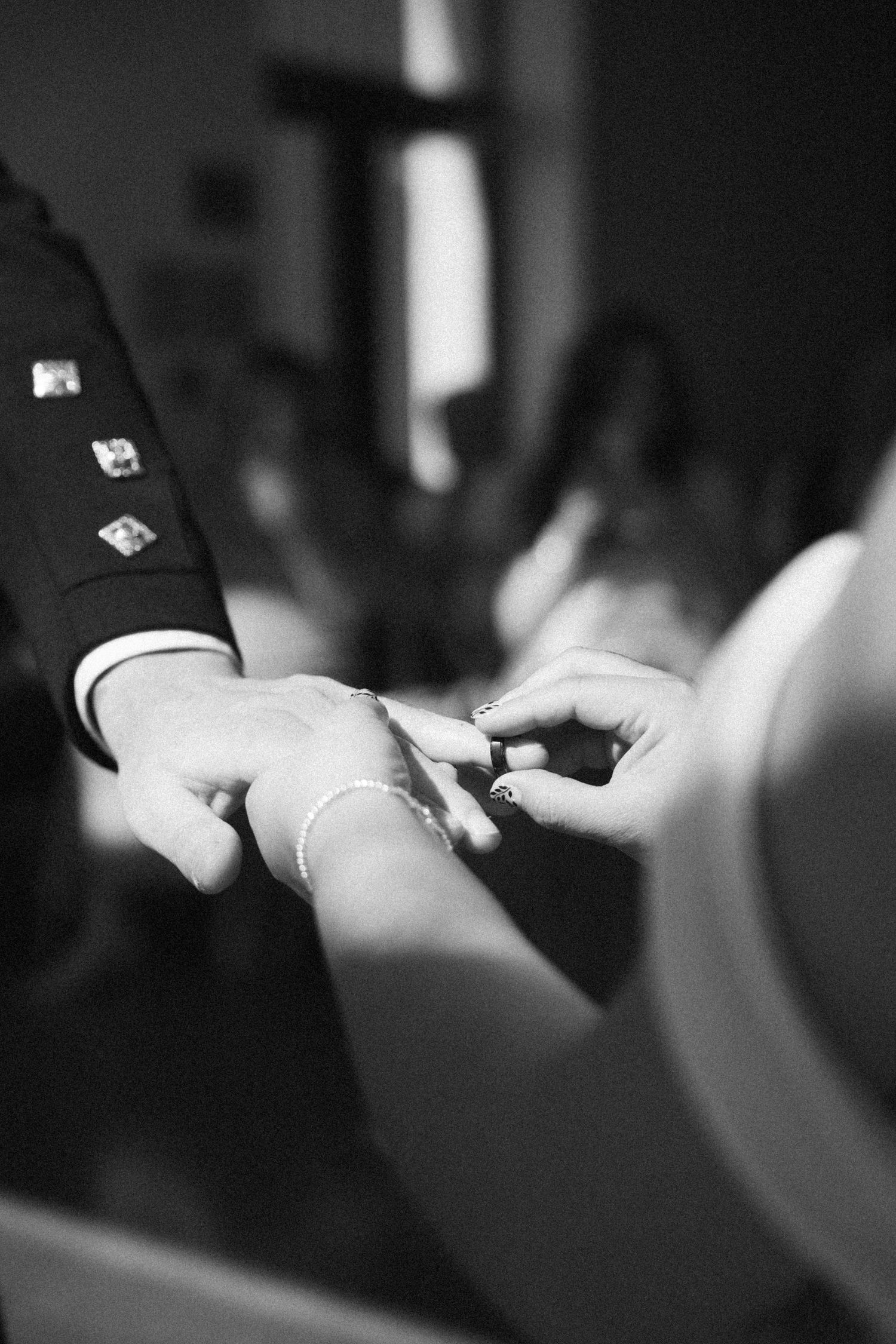 Close-up black and white photo of bride placing wedding ring on grooms hand during ceremony.