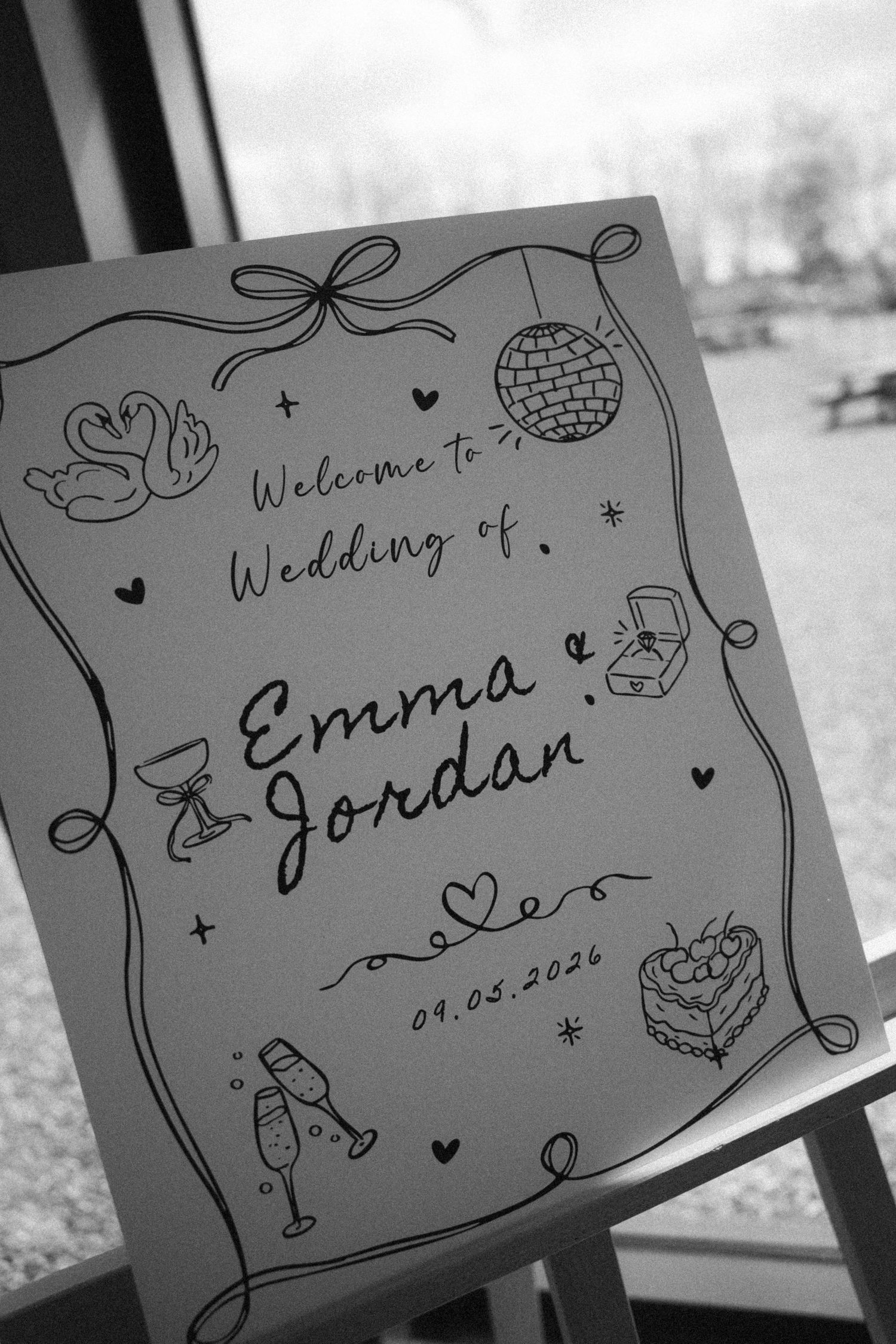 Black and white wedding welcome sign for Emma and Jordan, dated 09.05.2026, decorated with hand-drawn doodles.