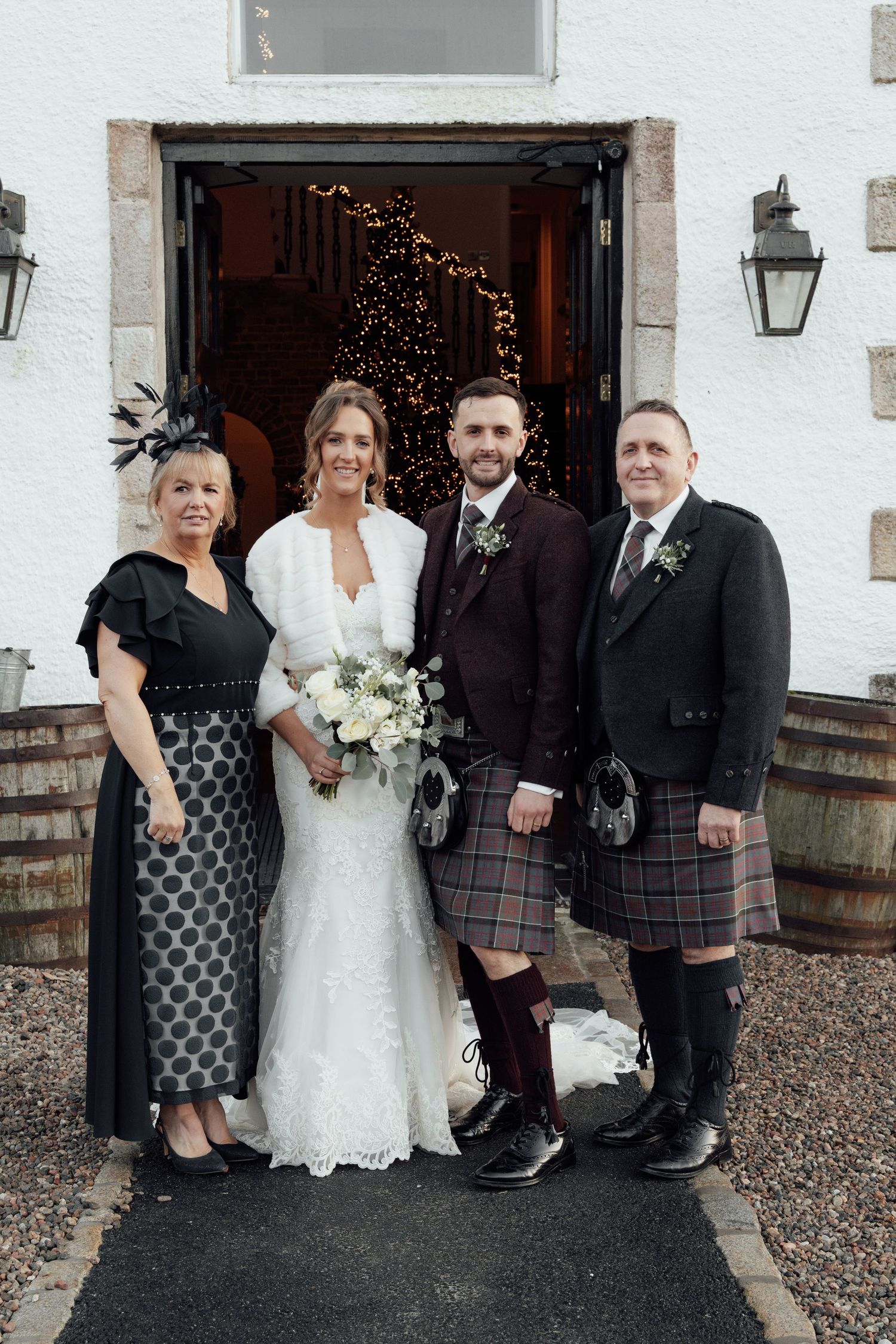 Scottish wedding party in formal attire gathered outside white building entrance.